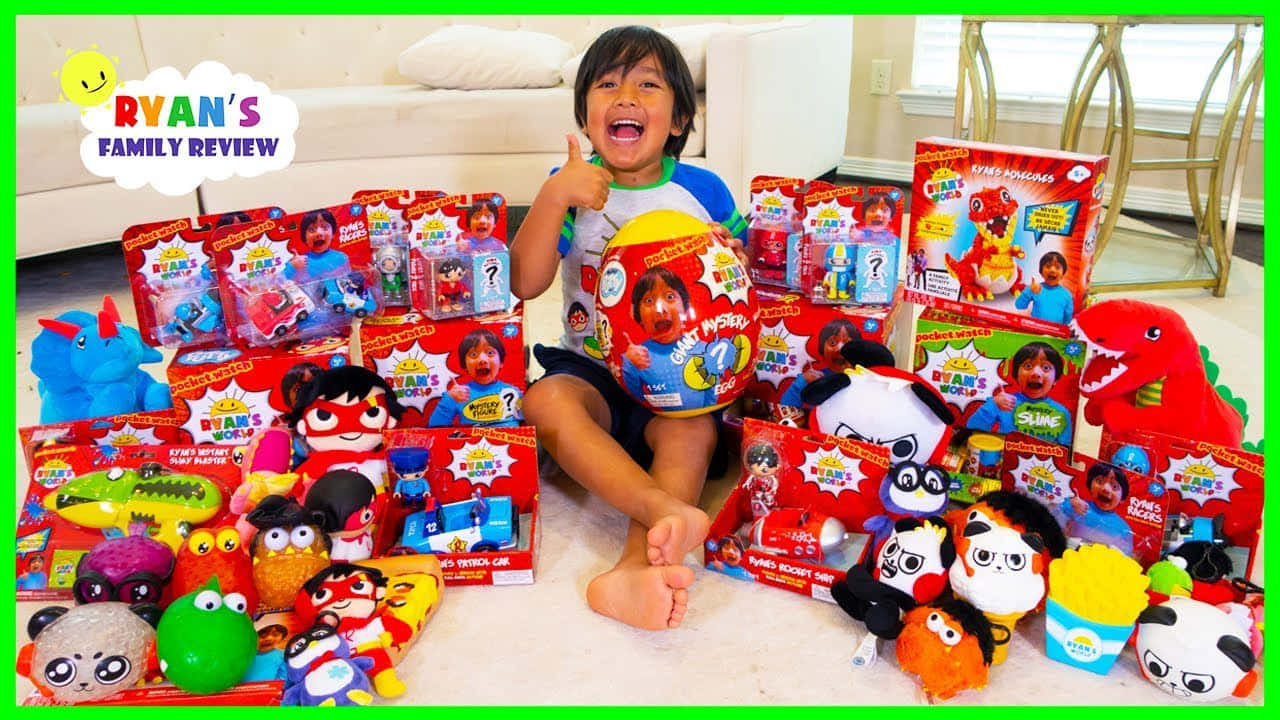 YouTube Banner 桌布 壁紙 — 一個快樂的孩子坐在地毯上，被色彩繽紛的Ryan's Family Review玩具和絨毛玩具包圍。