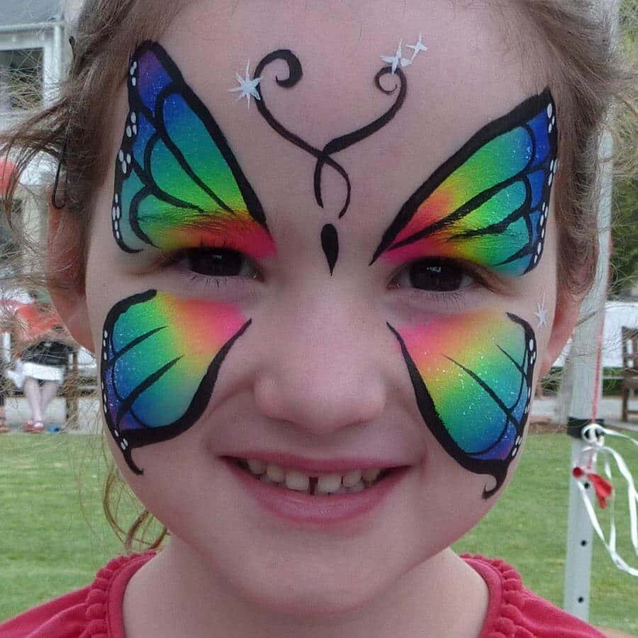 Butterfly Face Painting 桌布 壁紙 — 一個快樂的孩子微笑著，臉上畫著鮮豔的彩虹蝴蝶彩繪，背景是草地戶外。