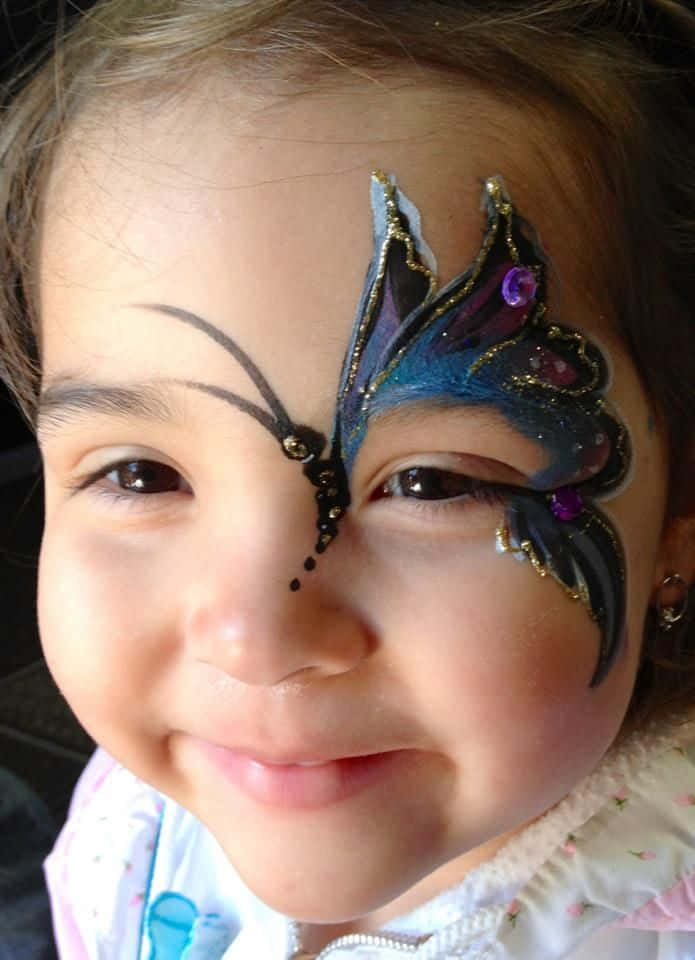 Butterfly Face Painting 桌布 壁紙 — 一個快樂的孩子微笑著，臉頰上畫著鮮豔的藍色和紫色蝴蝶。