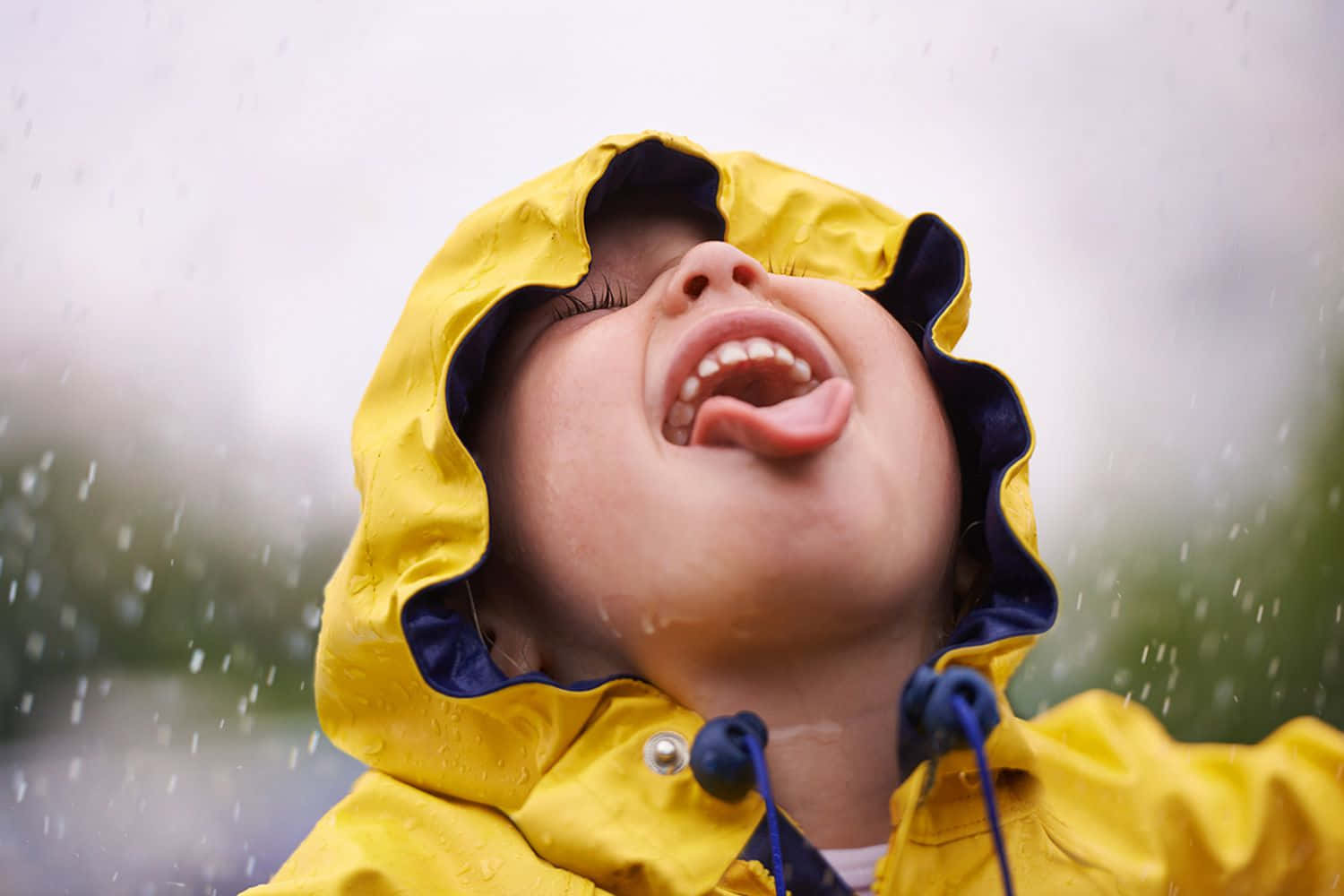 下雨 桌布 壁紙 — 一個快樂的孩子穿著黃色雨衣，伸出舌頭大笑，雨滴落在他們周圍。