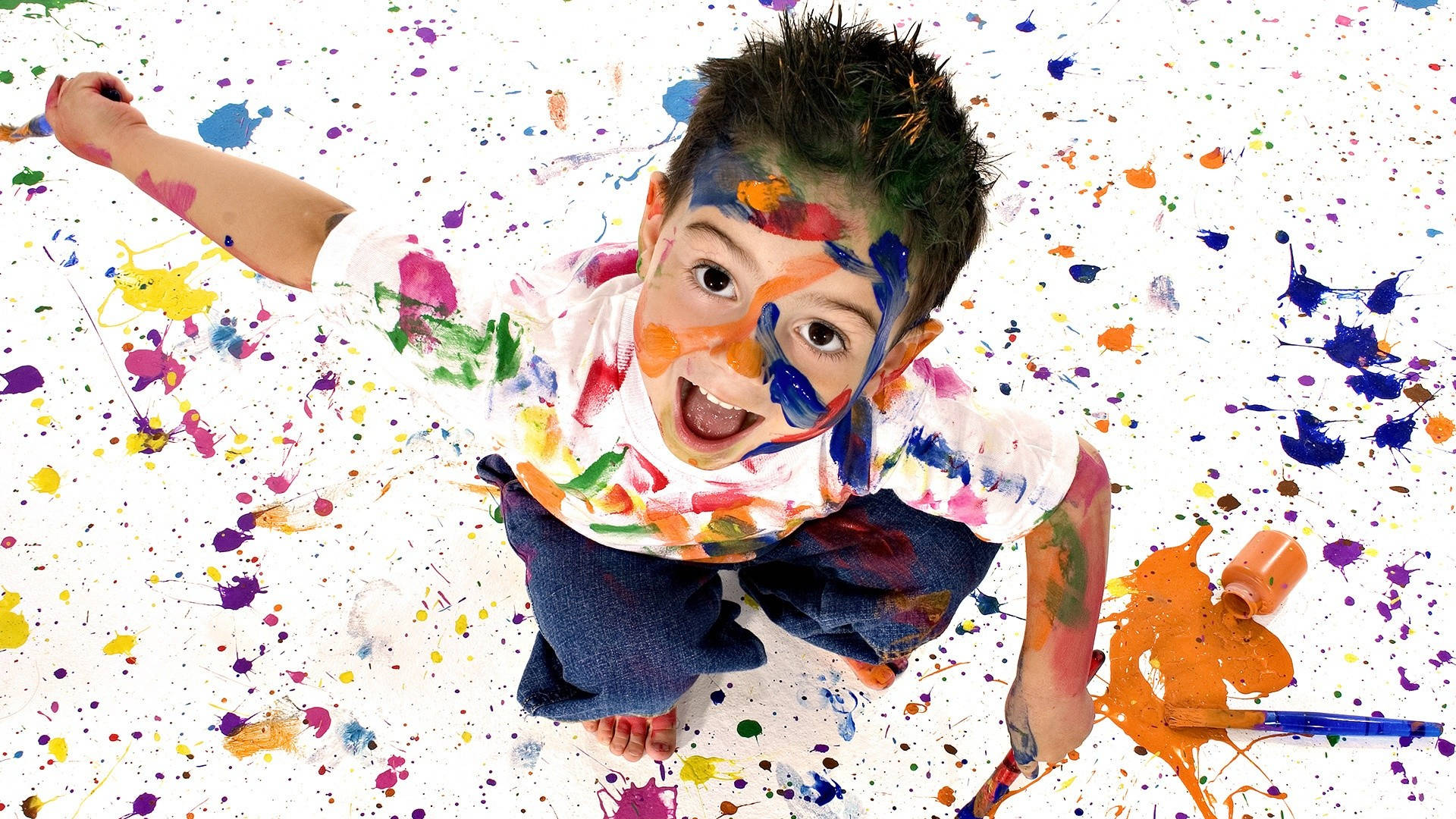 小孩動圖 桌布 壁紙 — 一個快樂的孩子身上佈滿了彩色油漆噴濺，在白色背景前抬頭露出燦爛的笑容。