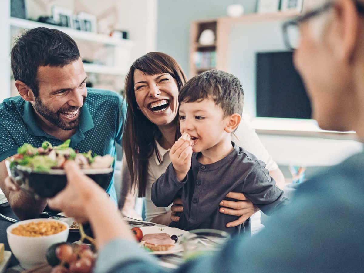 Family 桌布 壁紙 — 一個快樂的家庭在家裡一起分享一頓飯，桌上充滿笑聲和食物。
