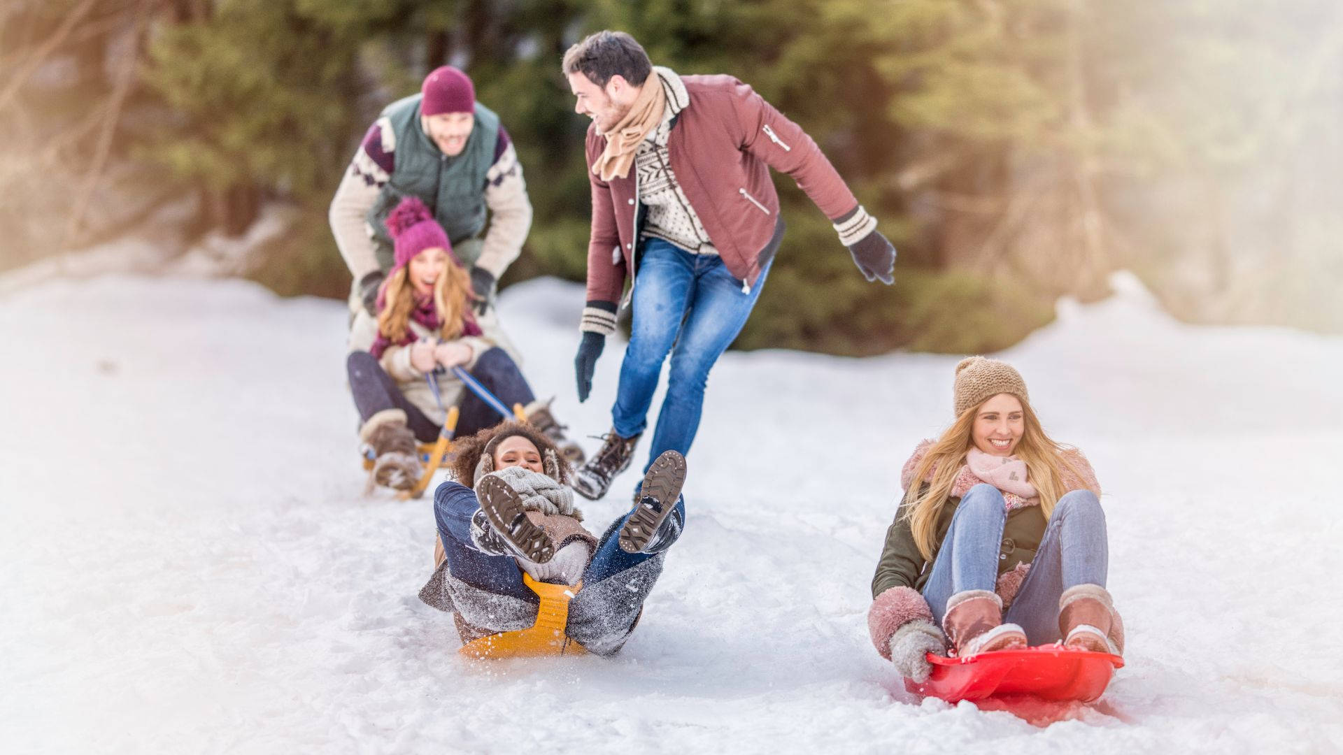 雪 桌布 壁紙 — 一個快樂的家庭在森林背景下，穿著鮮豔的冬季服裝，笑著滑雪橇下山坡。