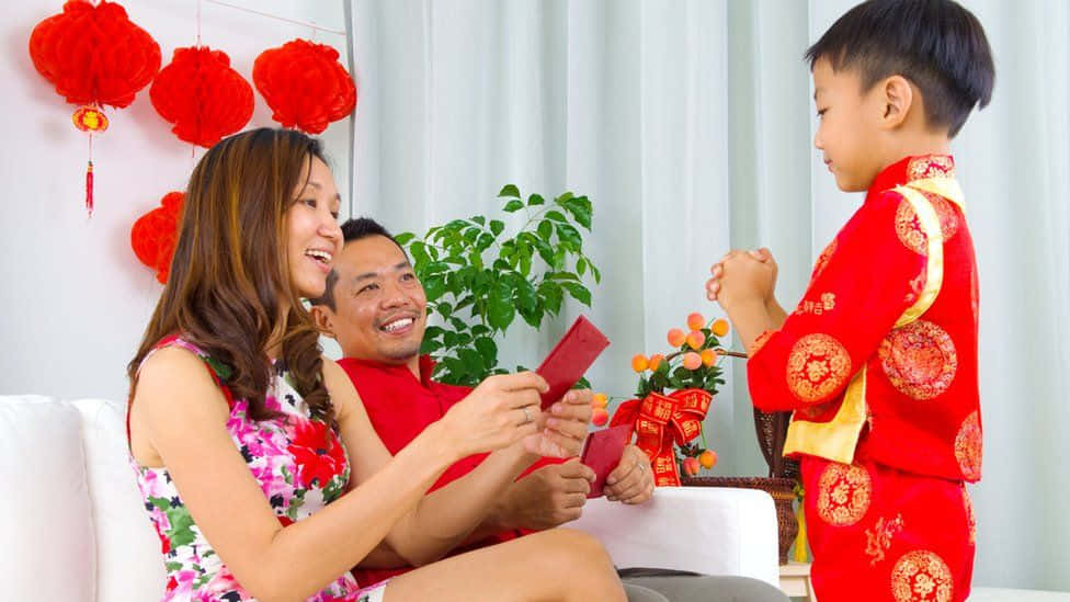 Red Envelope 桌布 壁紙 — 一個快樂的家庭慶祝農曆新年，父母給穿著喜慶紅色傳統服飾的微笑孩子發紅包。