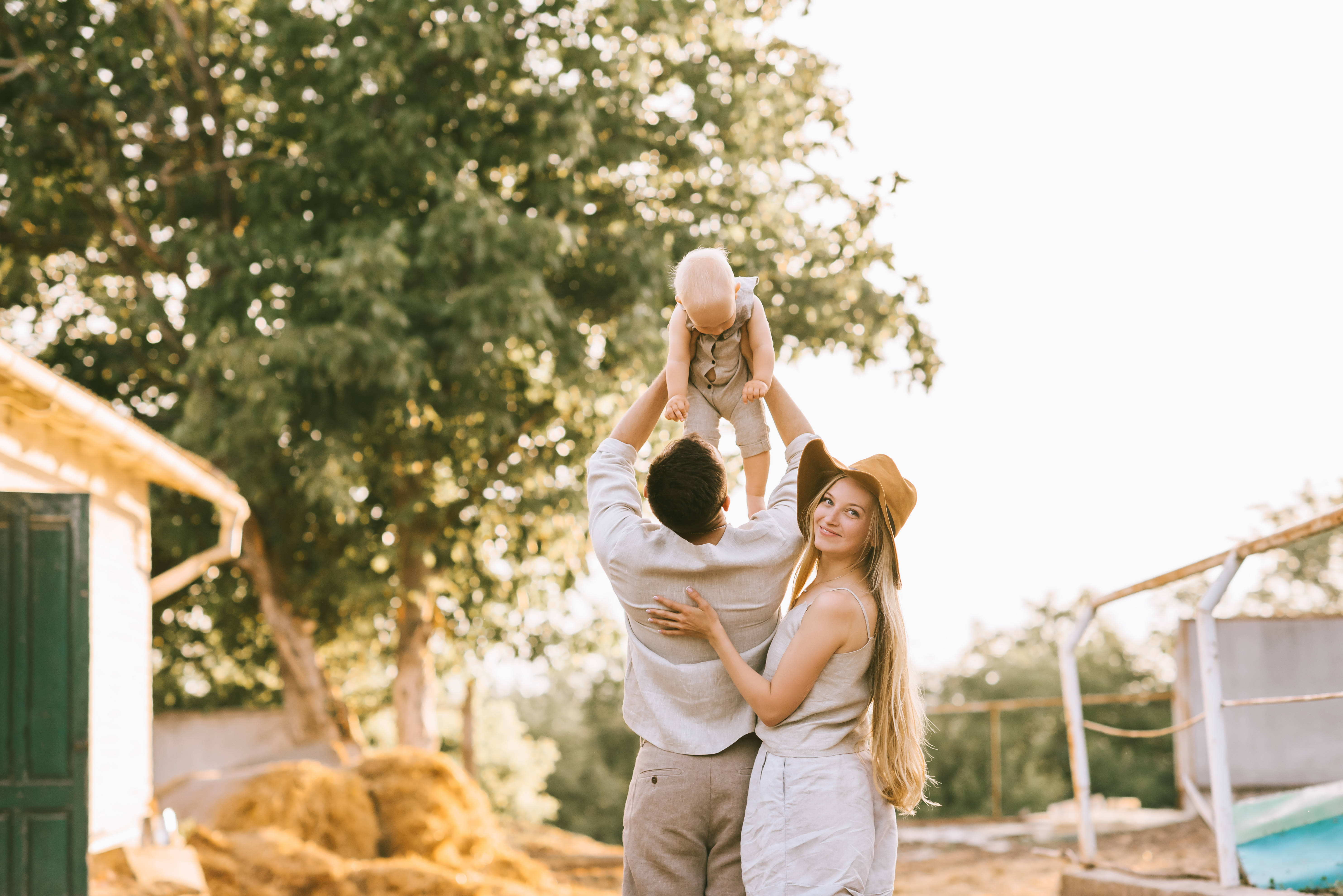 Family 桌布 壁紙 — 一個快樂的家庭時刻，父親高舉嬰兒，母親在金色陽光下微笑。