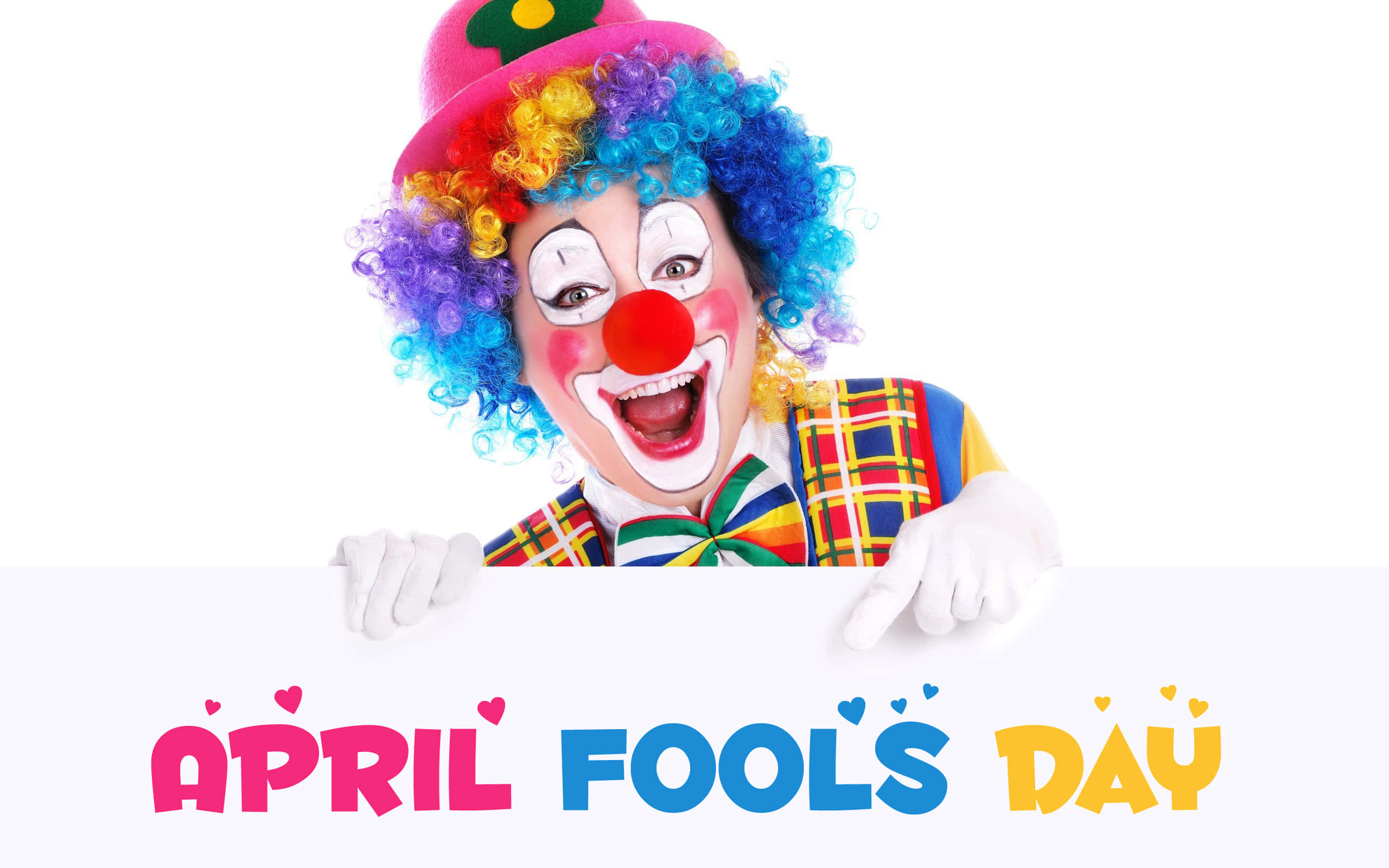 April Fools 桌布 壁紙 — 一個快樂的小丑，擁有彩虹色捲髮和紅鼻子，從一個寫著 April Fools Day 的標誌上方探出頭來。