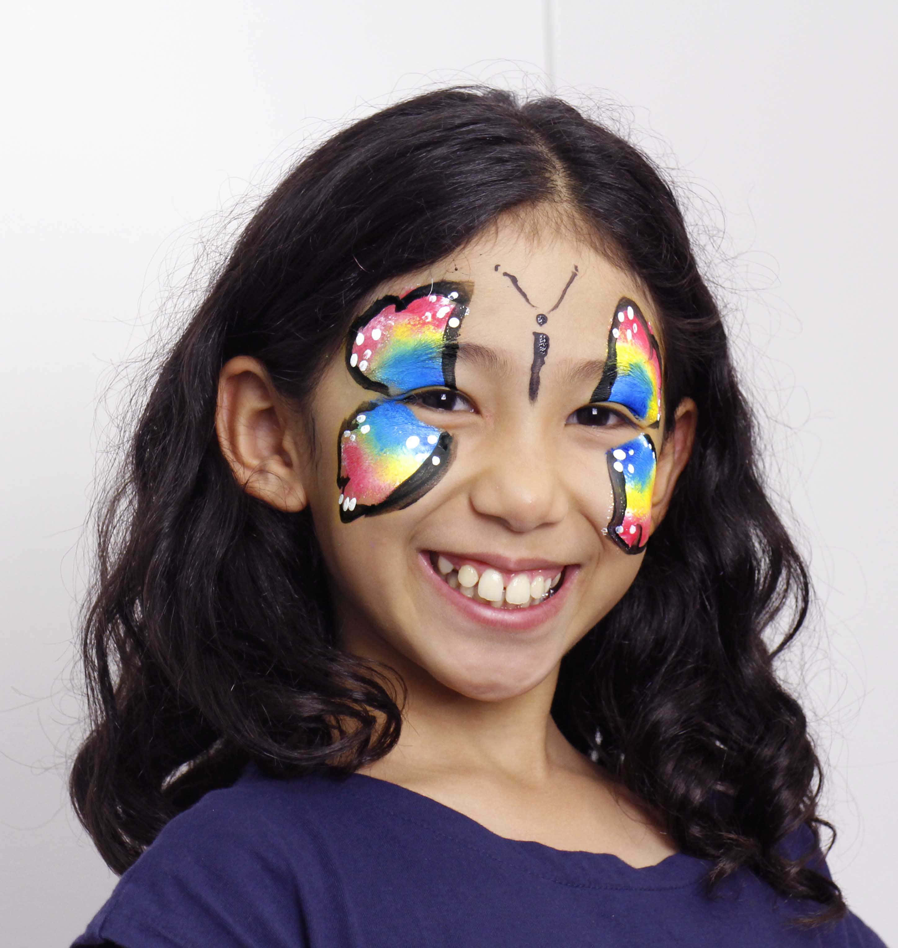 Butterfly Face Painting 桌布 壁紙 — 一個快樂的小女孩，臉上畫著鮮豔的彩虹蝴蝶彩繪，在純白背景前燦爛微笑。