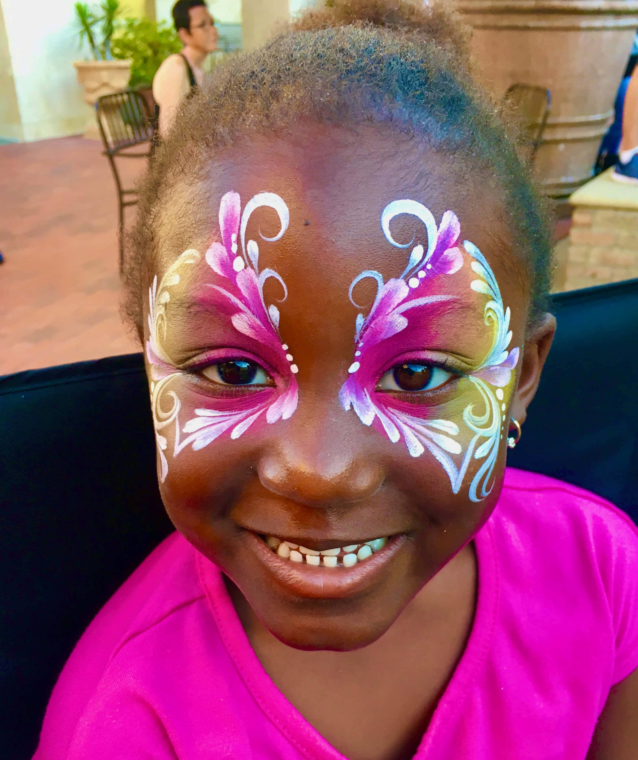 Butterfly Face Painting 桌布 壁紙 — 一個快樂的小女孩，臉上畫著鮮豔的蝴蝶圖案，在陽光明媚的戶外環境中燦爛地微笑。
