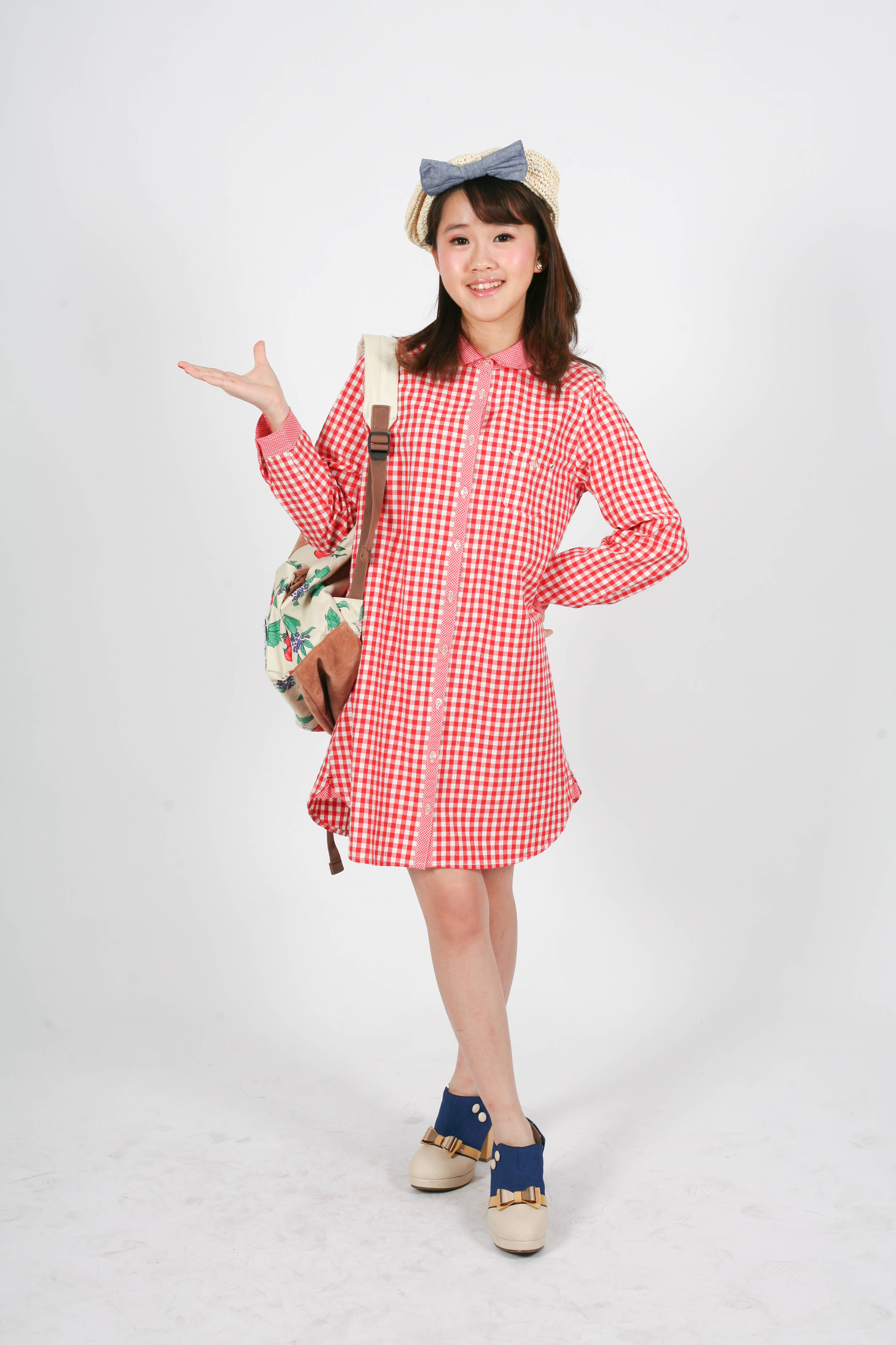可愛粉色動圖 桌布 壁紙 — 一個快樂的小女孩穿著紅色格子連衣裙和草帽，背著花卉圖案背包，在純白色工作室背景前擺姿勢。