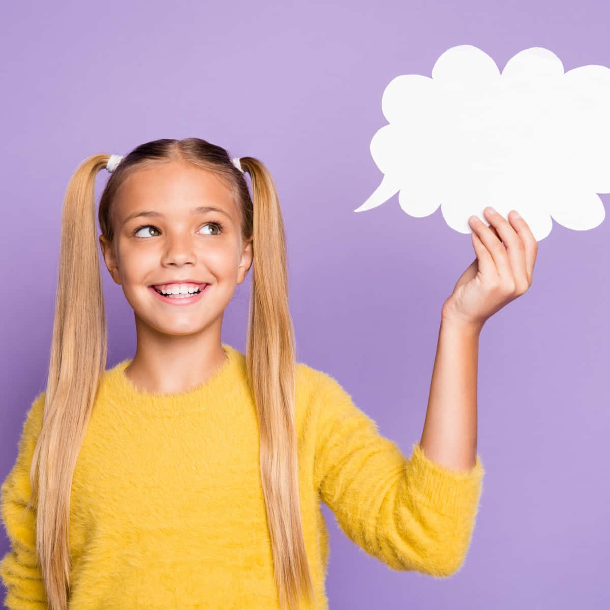 Speech Bubble 桌布 壁紙 — 一個快樂的年輕女孩穿著毛茸茸的黃色毛衣，在柔和的紫色背景前拿著一個空白的白色對話框。