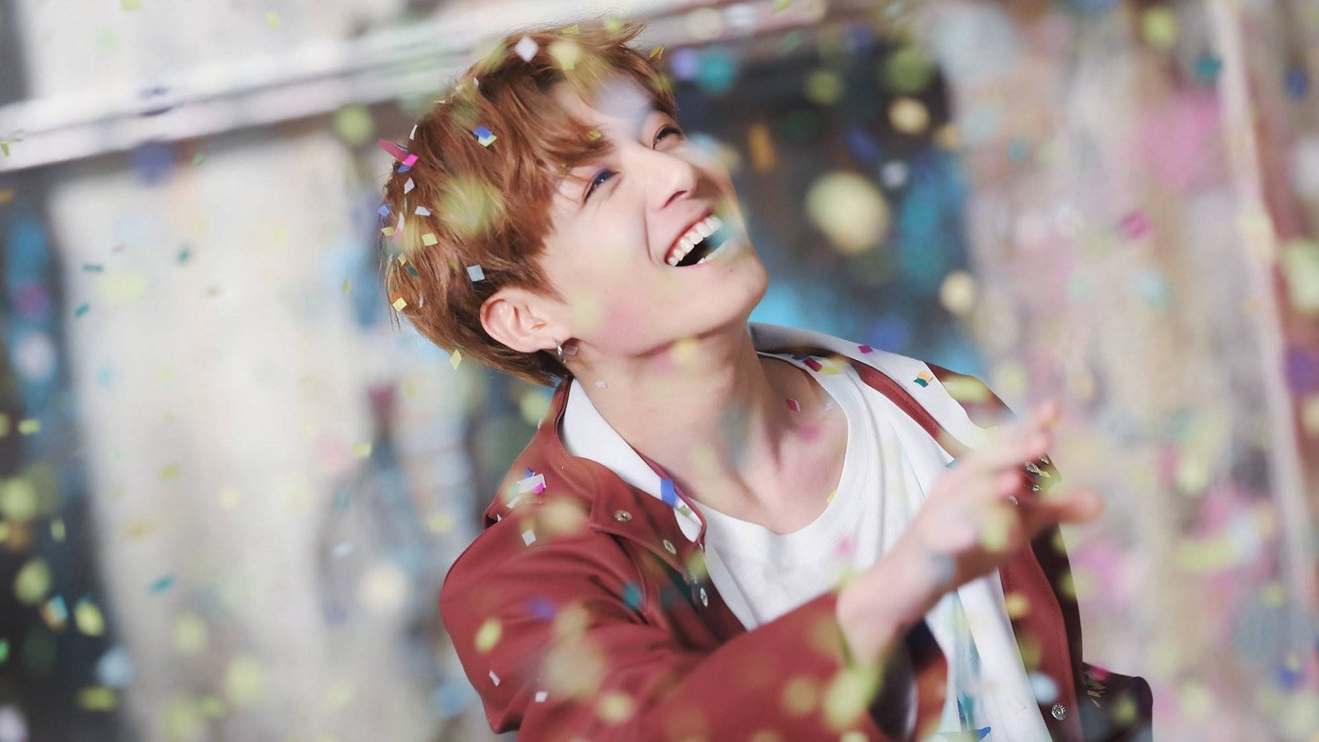 Jungkook 桌布 壁紙 — 一個快樂的年輕男子閉著眼睛大笑，彩色紙屑如雨般落在他周圍，在明亮的慶祝活動中。