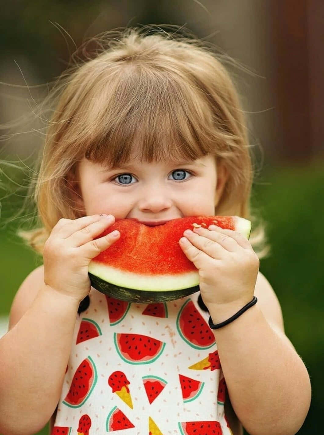 Watermelon 桌布 壁紙 — 一個快樂的幼兒，有著明亮的藍眼睛，在戶外開心地吃著多汁的西瓜片。