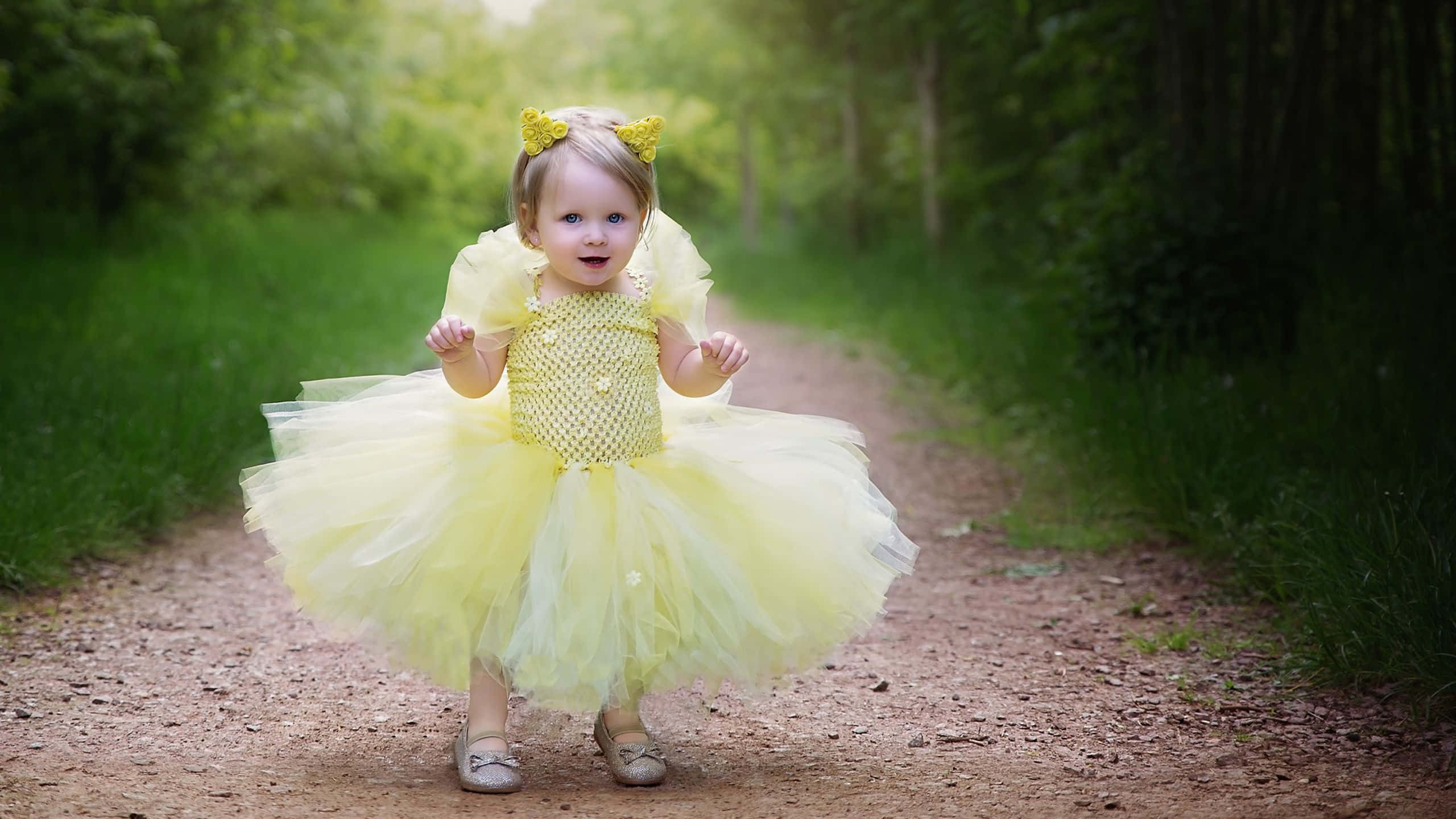 Yellow Dress 桌布 壁紙 — 一個快樂的幼兒穿著亮黃色薄紗裙和相配的頭帶，走在陽光灑落的森林小徑上。