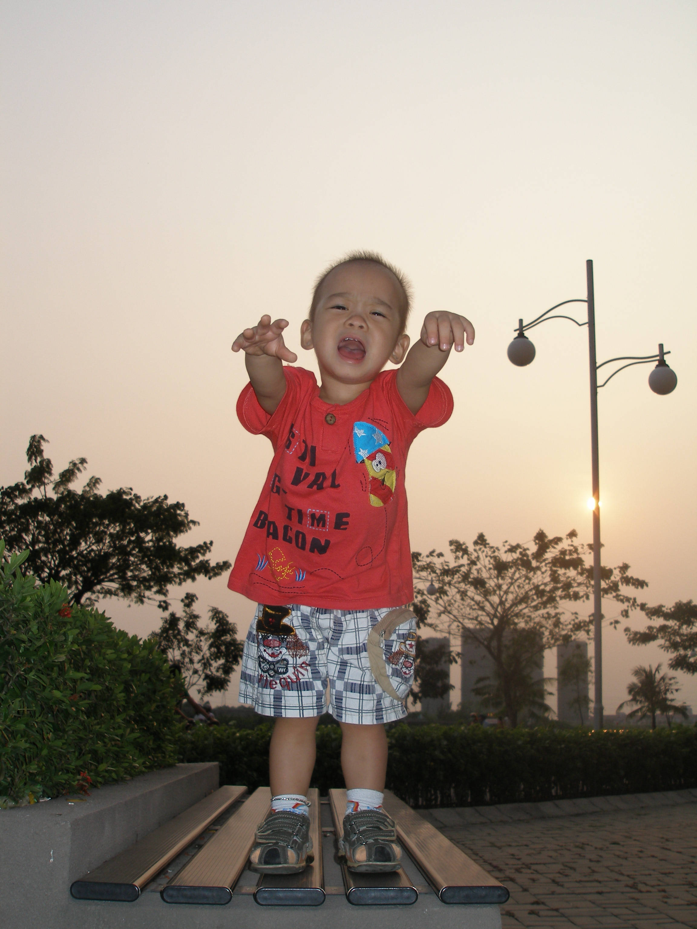 crying sad boy 桌布 壁紙 — 一個快樂的幼兒穿著紅色襯衫，在日落時站在戶外的金屬條上，雙臂張開，嘴巴張開，充滿喜悅。