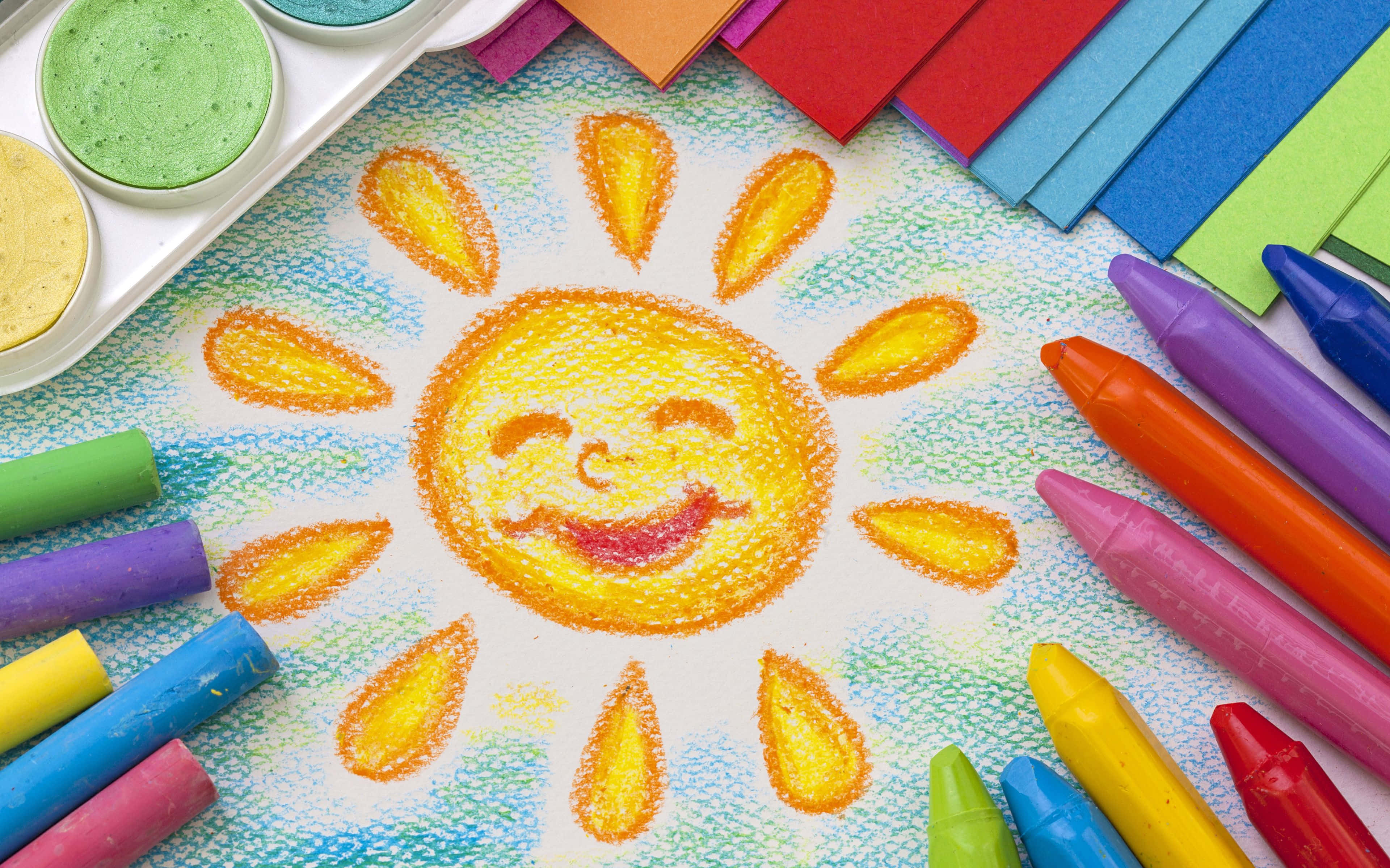 crayon 桌布 壁紙 — 一個快樂的手繪太陽，帶著笑臉，在紋理紙上被色彩繽紛的蠟筆和調色板包圍，散發溫暖。