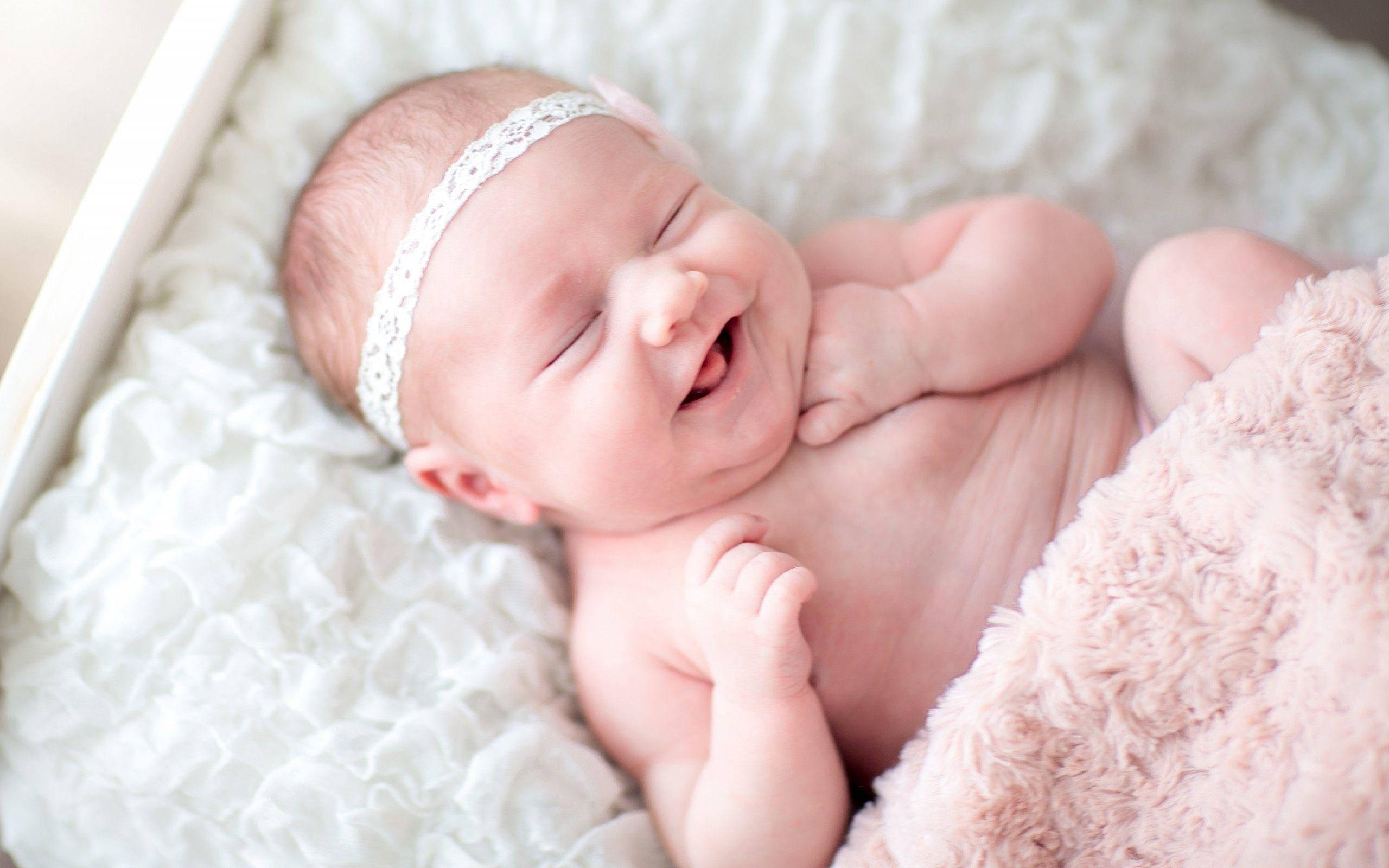 Baby Girl 桌布 壁紙 — 一個快樂的新生嬰兒閉著眼睛大笑，被柔軟的粉紅色和白色紋理毯子包裹著。