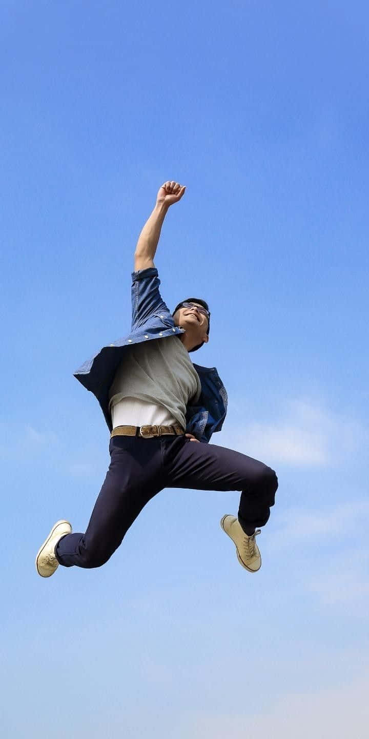 jump 桌布 壁紙 — 一個快樂的男人在晴朗的藍天下高舉拳頭，高高躍起，充滿勝利感。