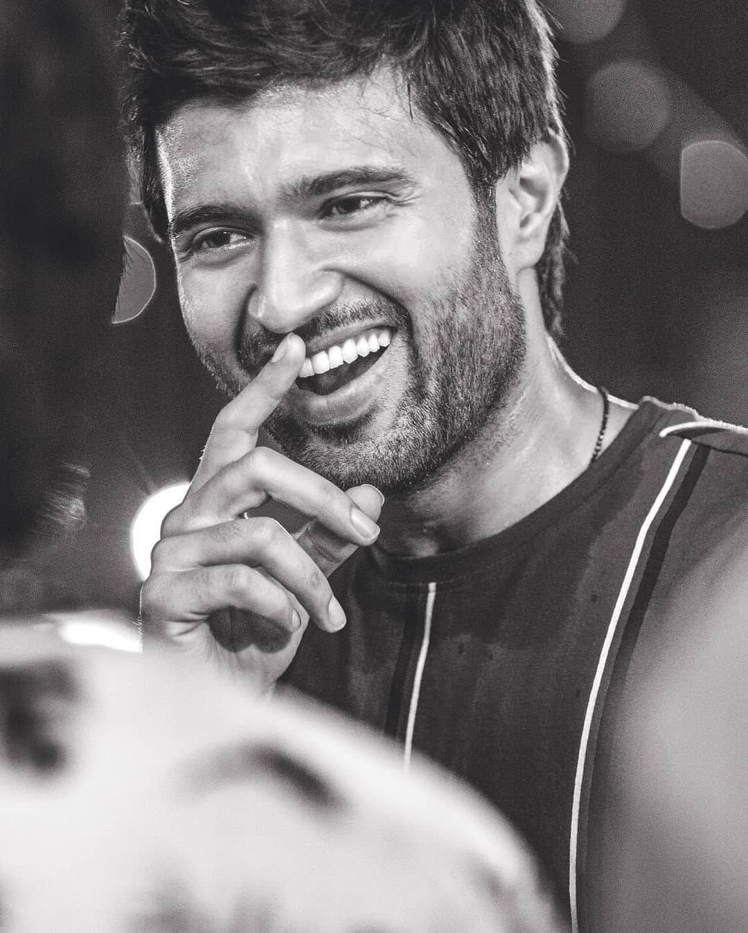vijay devarakonda 4K 桌布 壁紙 — 一個快樂的男人在黑白照片中，手指放在嘴唇上笑著，同時抱著一個足球。