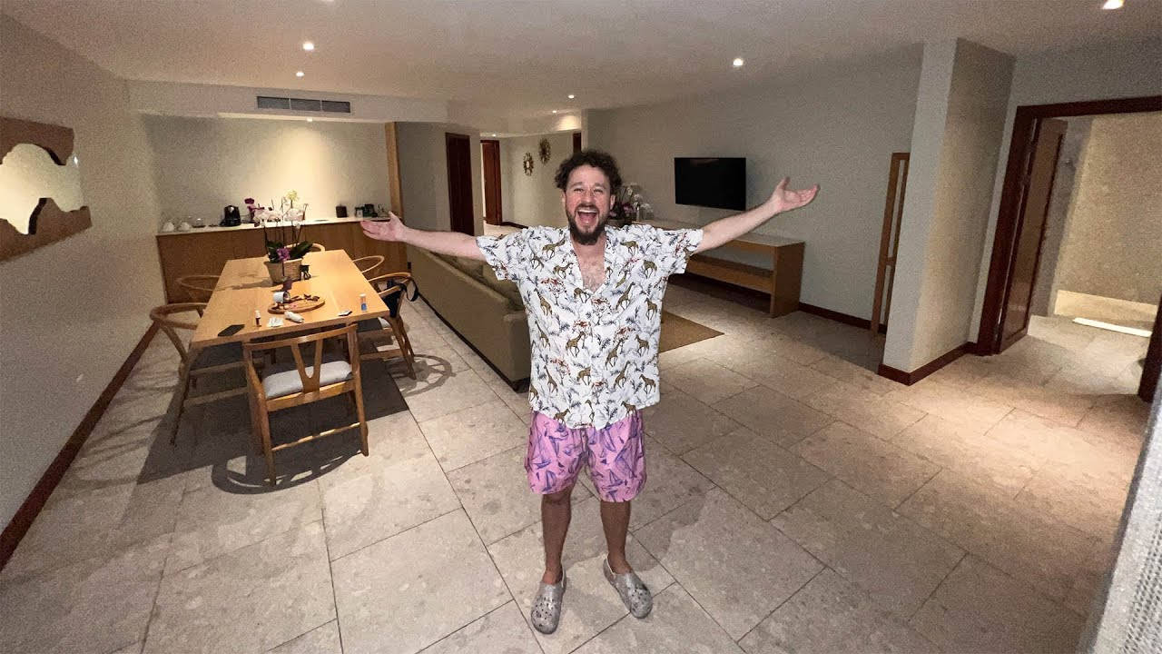 快樂 桌布 壁紙 — 一個快樂的男人張開雙臂站在現代瓷磚客廳裡，配有木製家具和溫暖的燈光。