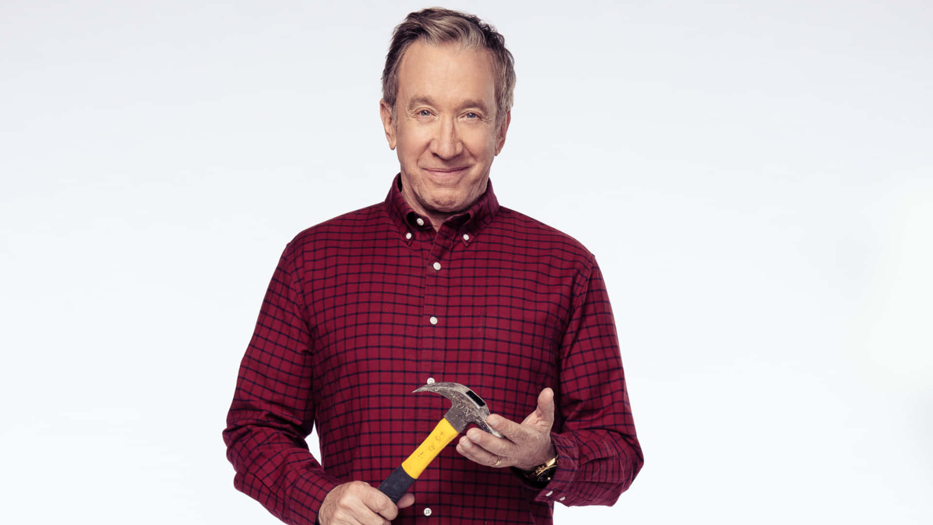 Tim Allen 桌布 壁紙 — 一個快樂的男人穿著紅色格紋襯衫，在純白色背景前拿著一把羊角錘。