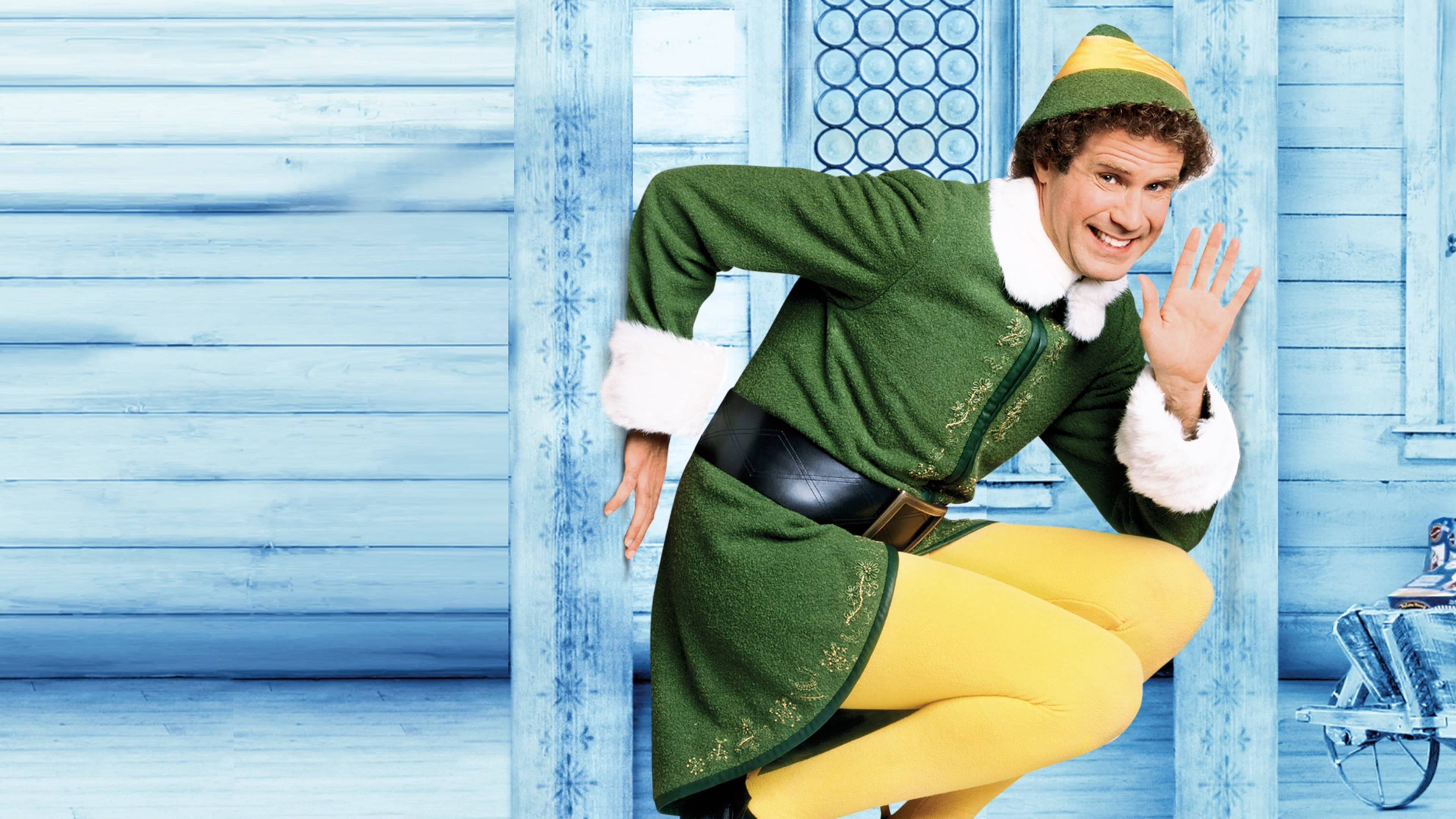 will ferrell 桌布 壁紙 — 一個快樂的男人穿著綠色和黃色的精靈服裝，在帶有雪花裝飾的藍色木質門廊上揮手。