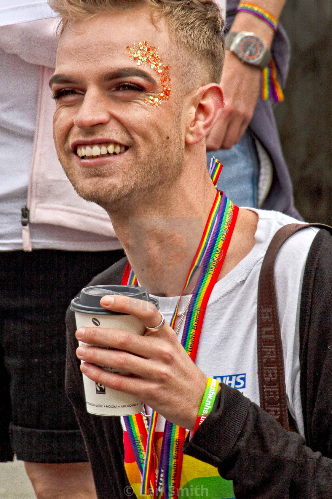 smiling 桌布 壁紙 — 一個快樂的男人臉頰上有亮粉，在Pride活動中拿著咖啡杯微笑。