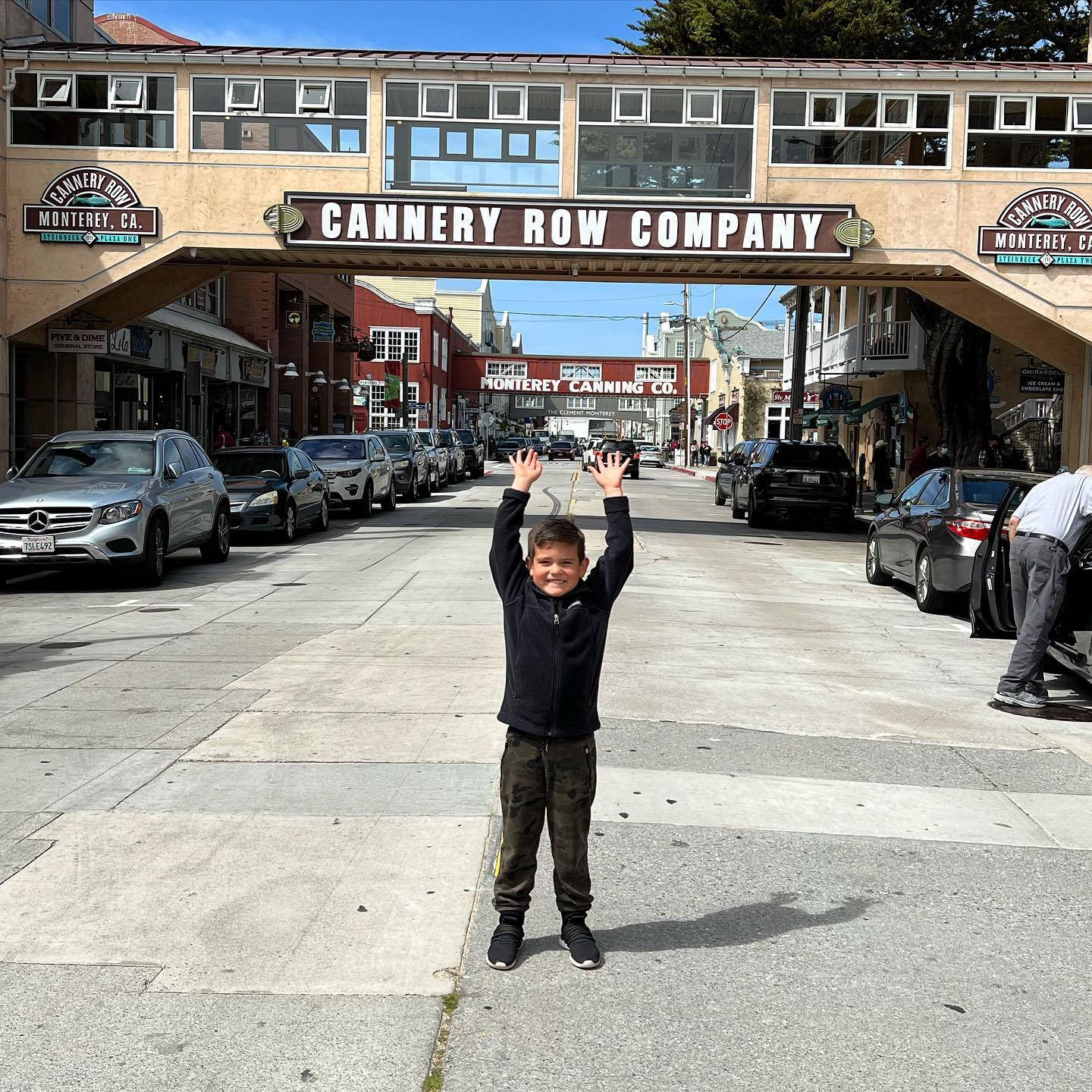 Boy 桌布 壁紙 — 一個快樂的男孩舉起雙臂，站在加州蒙特雷的Cannery Row Company拱門下的陽光街道上。