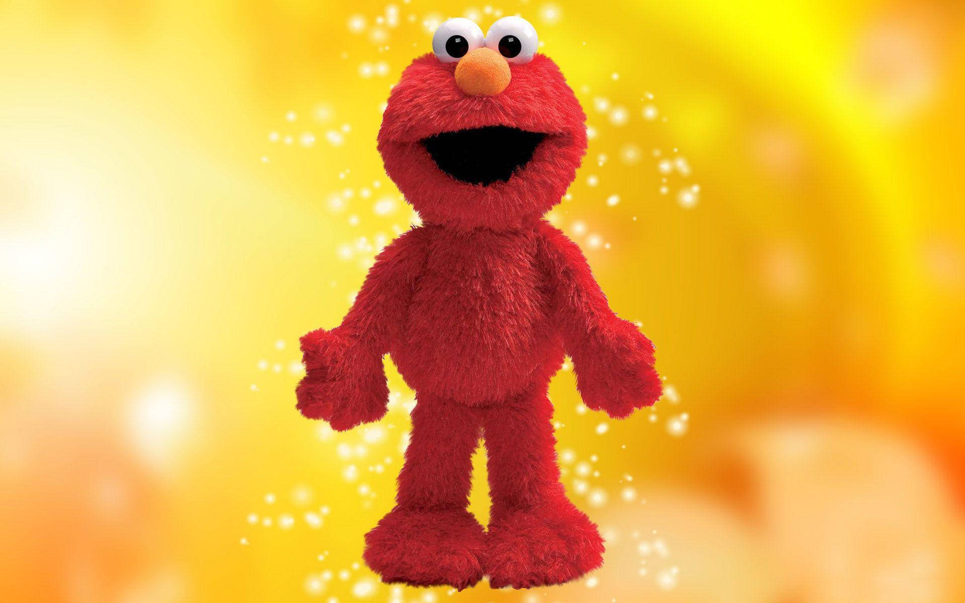 Elmo 桌布 壁紙 — 一個快樂的紅色毛絨Elmo公仔在閃爍的金色背景上燦爛地微笑，帶有閃爍的粒子。