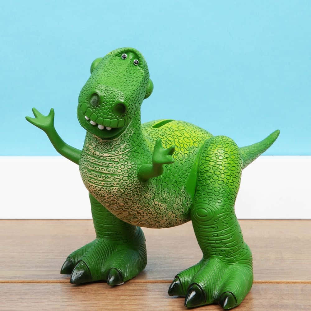 Toy Story 4 桌布 壁紙 — 一個快樂的綠色塑膠恐龍玩具，帶有紋理皮膚和背部的硬幣槽，站在木質表面上，對著藍白背景揮手。
