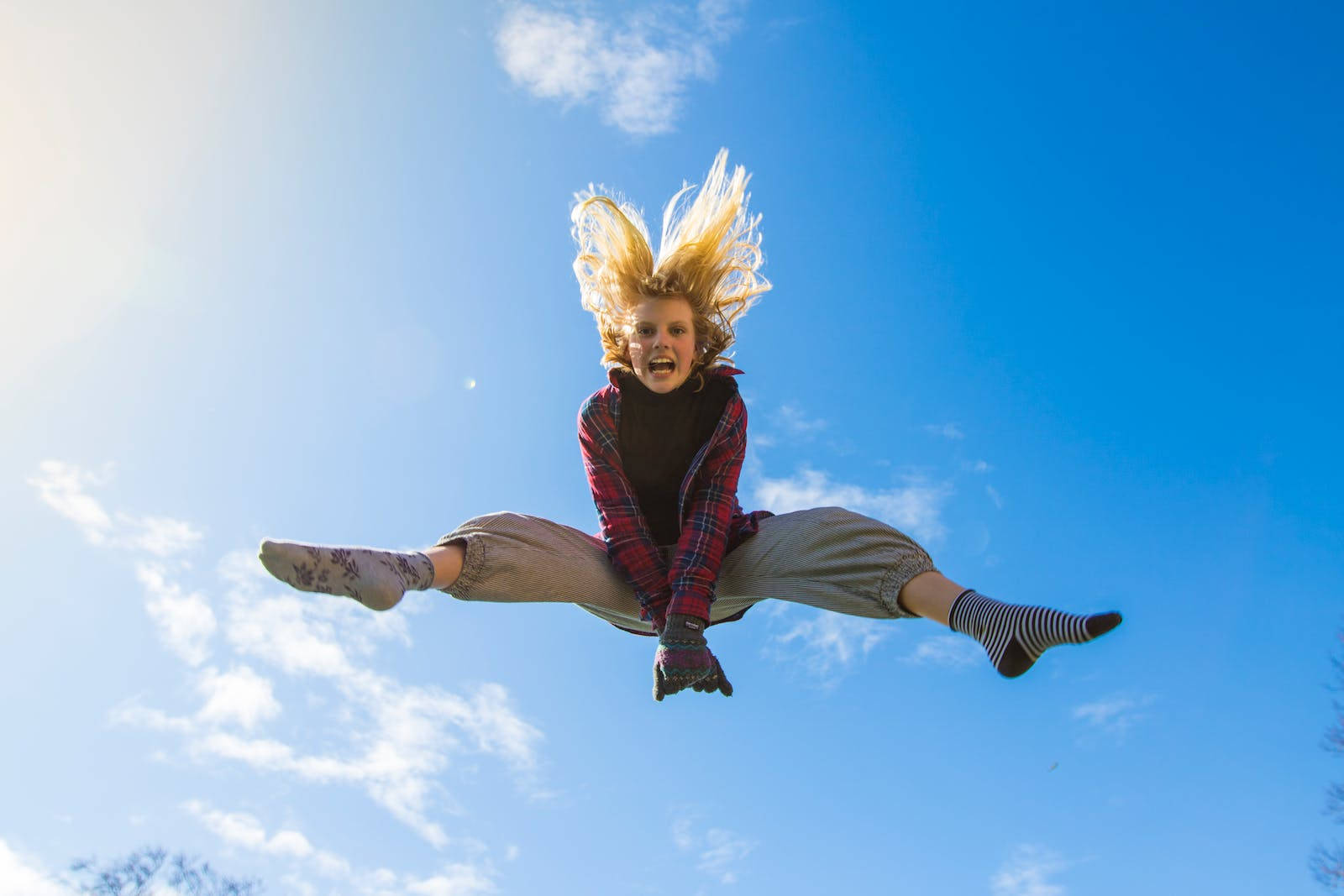 Jumping 桌布 壁紙 — 一個快樂的金髮女孩在明亮的藍天白雲中飛翔。