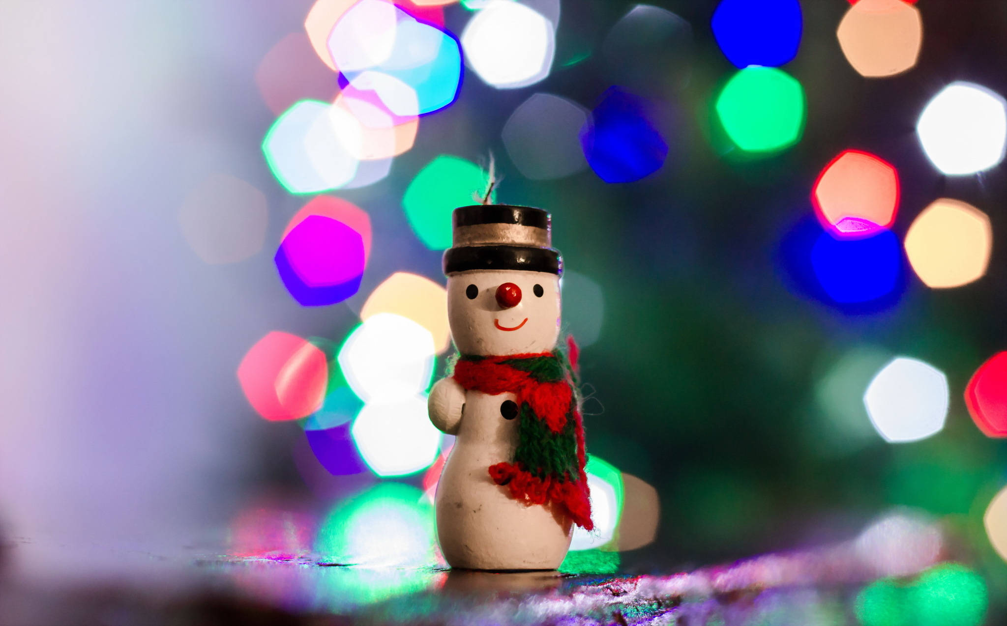 雪人 桌布 壁紙 — 一個快樂的雪人公仔，紅鼻子和圍巾，站在充滿活力的節日燈光散景前。
