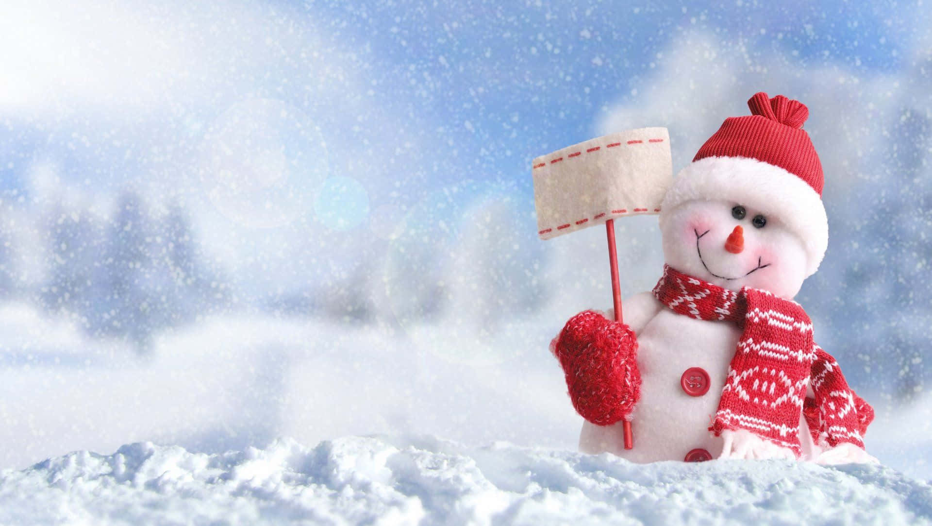 冬季聖誕 桌布 壁紙 — 一個快樂的雪人戴著紅色帽子、圍巾和手套，站在雪景中舉著一個牌子。