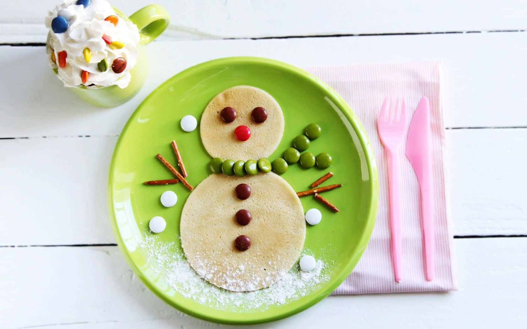 Winter Desserts 桌布 壁紙 — 一個快樂的雪人煎餅放在綠色盤子上，用糖果眼睛、椒鹽脆餅手臂和糖粉雪裝飾。