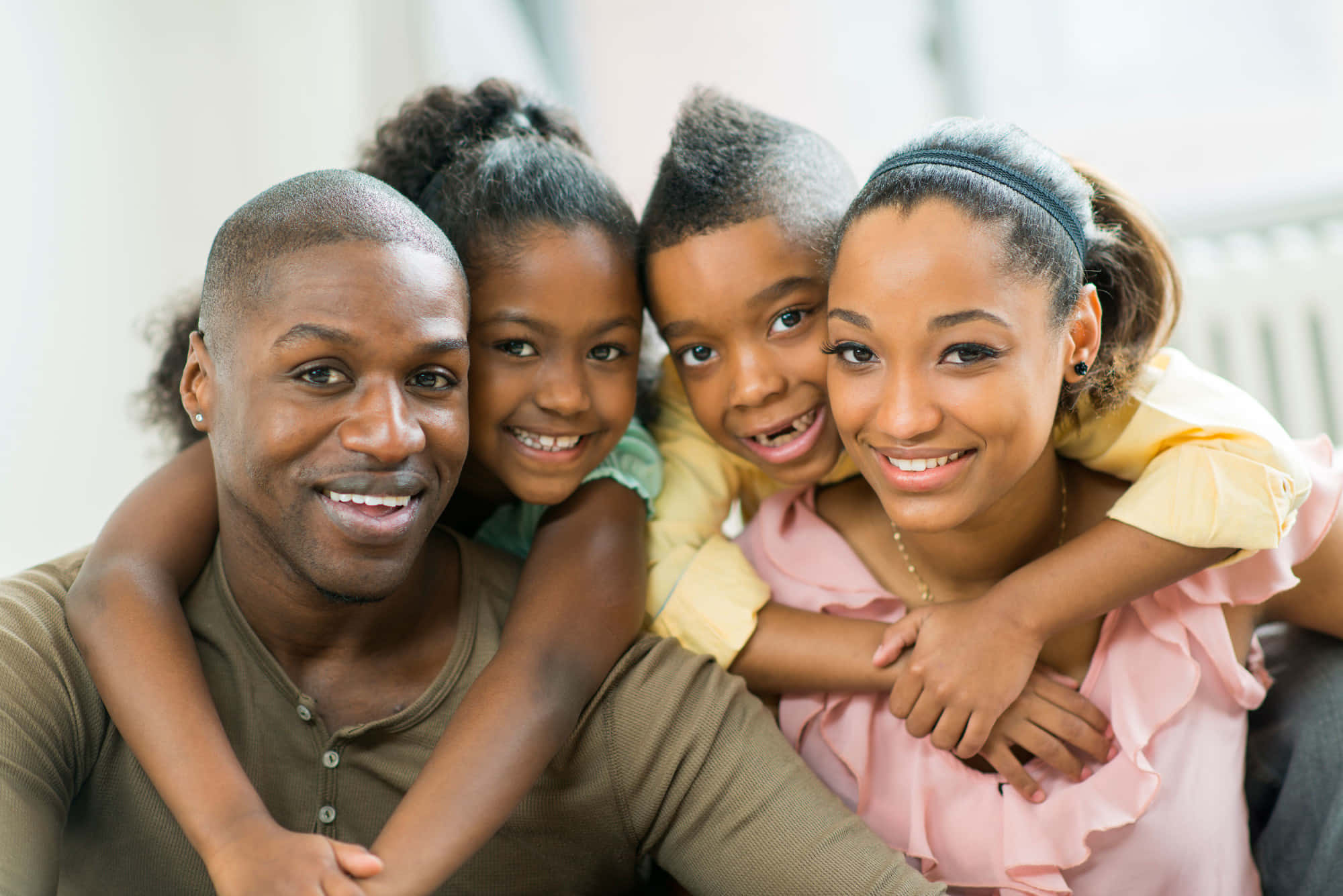 Black Family 桌布 壁紙 — 一個快樂的非裔美國四人家庭在室內緊緊擁抱，溫暖地微笑。