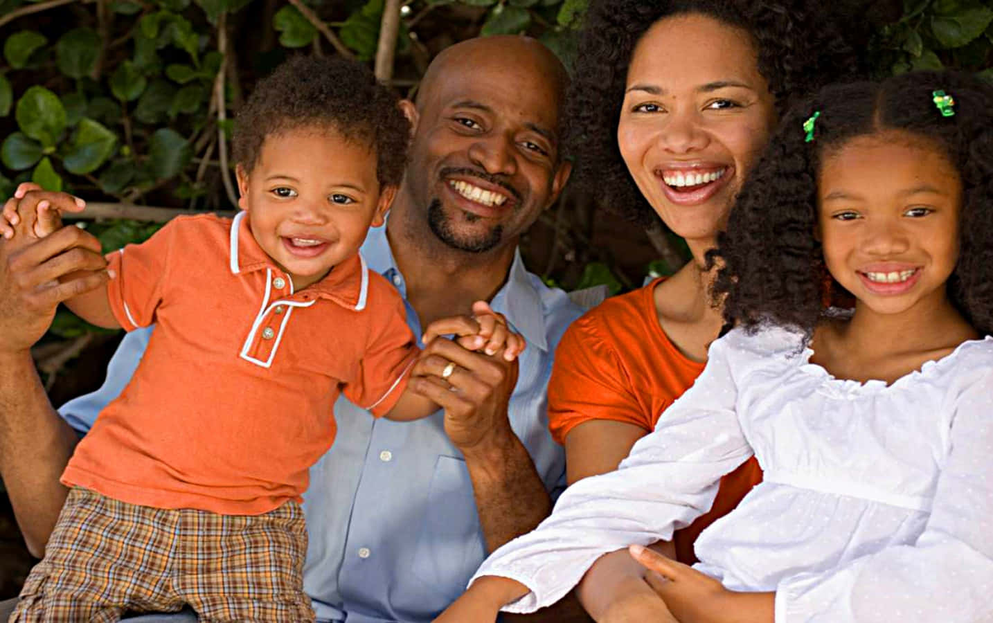 Black Family 桌布 壁紙 — 一個快樂的非裔美國四人家庭在戶外綠葉下牽手微笑。