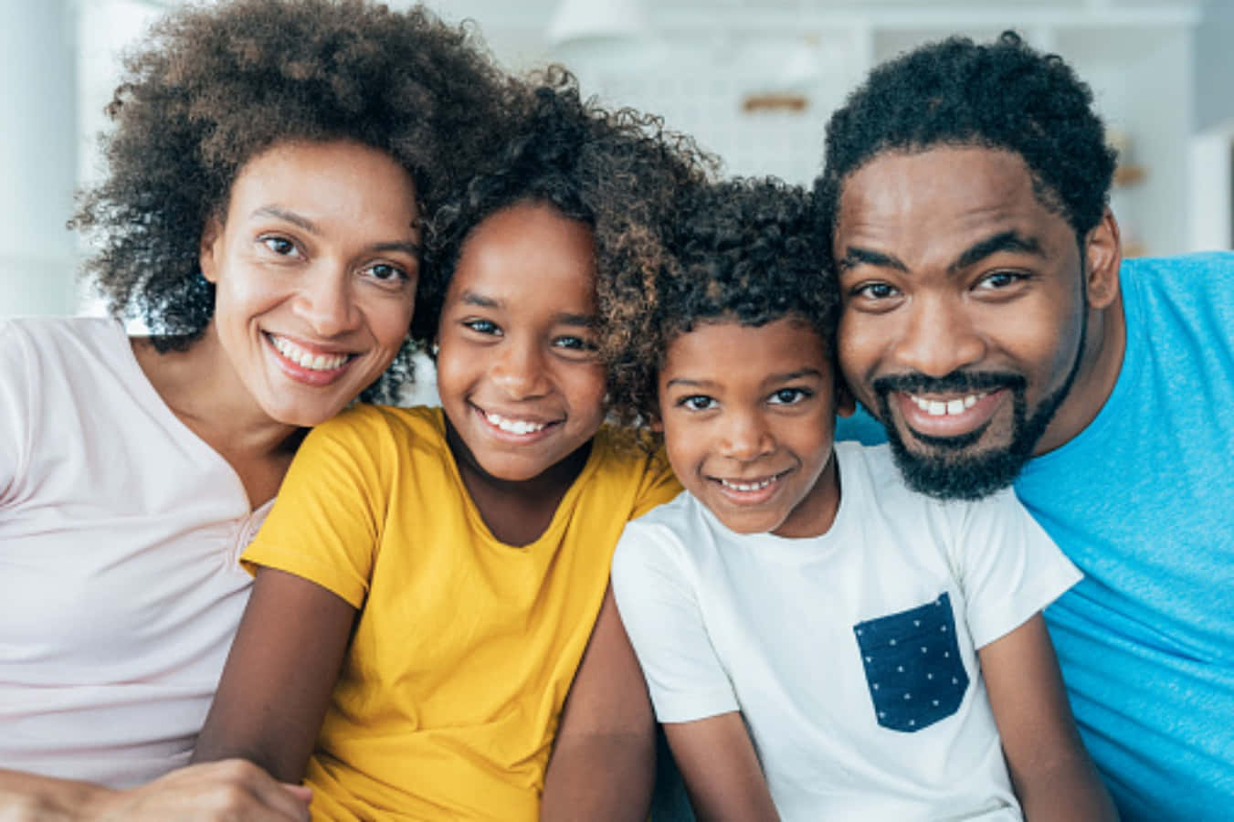 Black Family 桌布 壁紙 — 一個快樂的非裔美國四人家庭在明亮的室內環境中對著鏡頭溫暖地微笑。