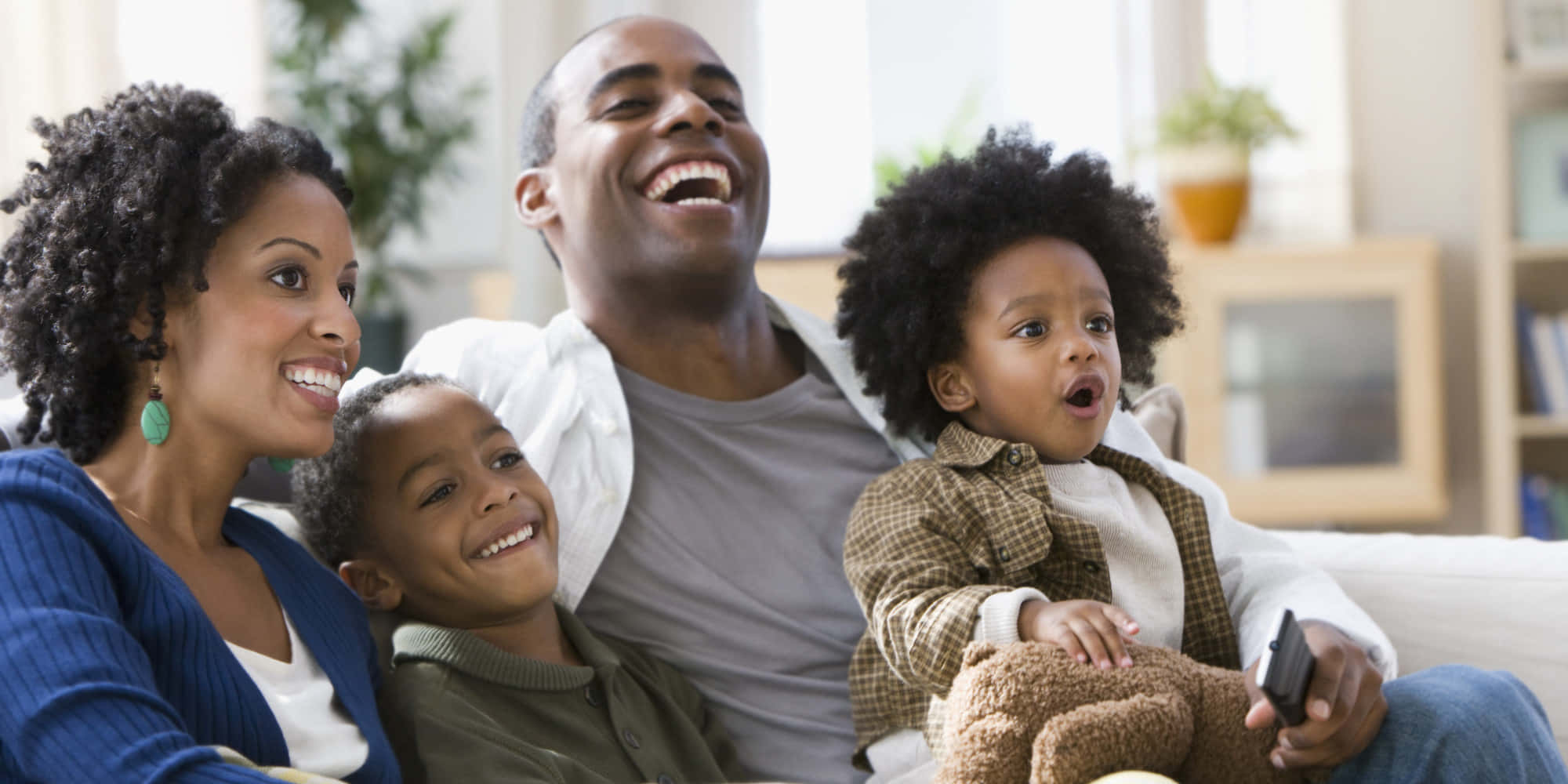 Black Family 桌布 壁紙 — 一個快樂的非裔美國四人家庭在明亮的客廳沙發上一起大笑。