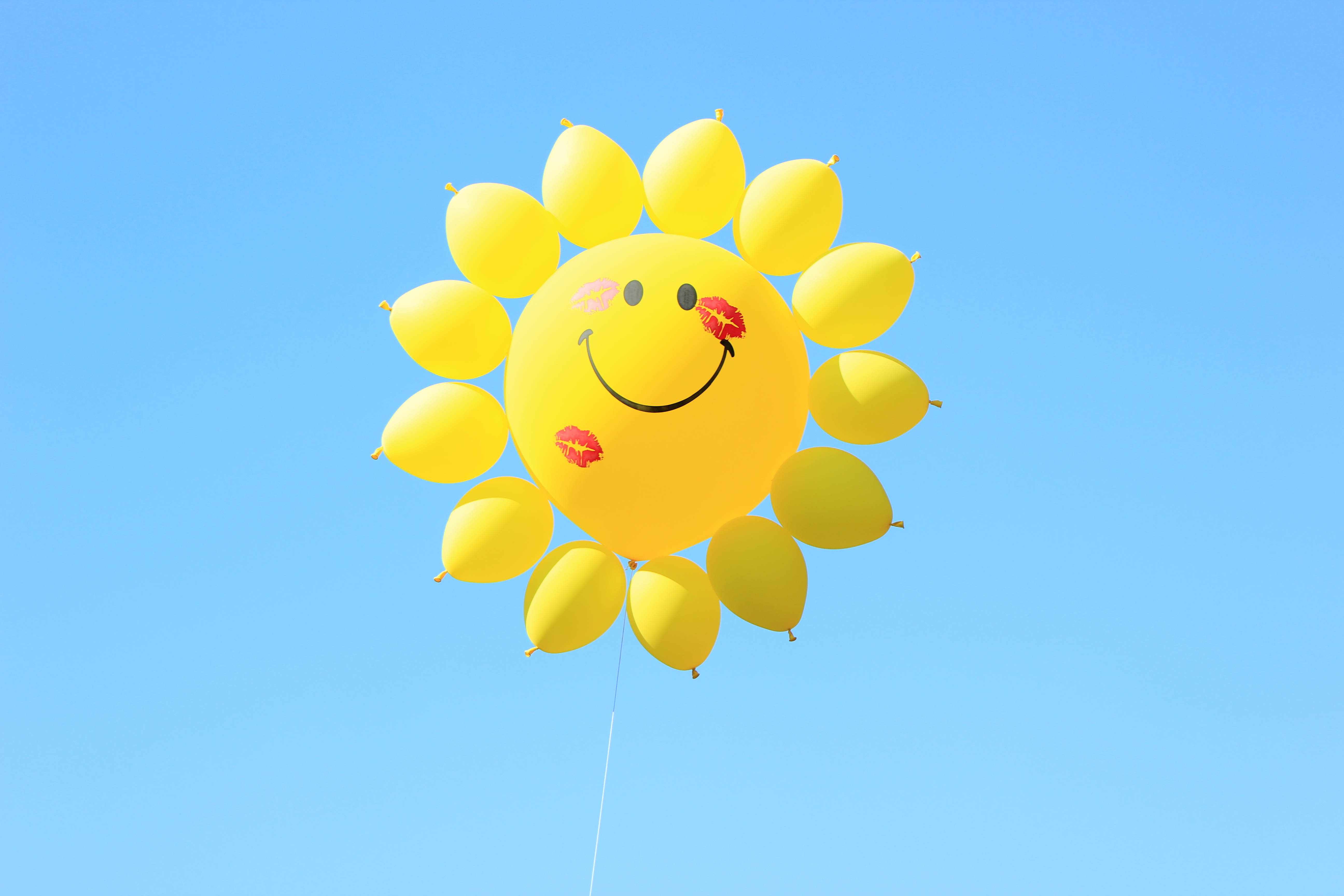 Smile 桌布 壁紙 — 一個快樂的黃色氣球，形狀像微笑的太陽，帶有紅色唇膏吻痕，漂浮在清澈的藍天上。