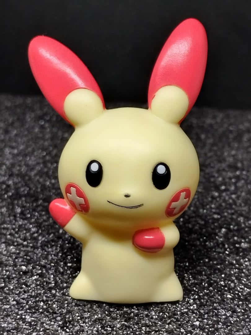 Pokemon Aesthetic 桌布 壁紙 — 一個快樂的黃色皮卡丘公仔，有紅色耳朵和臉頰，站在深色紋理表面上。
