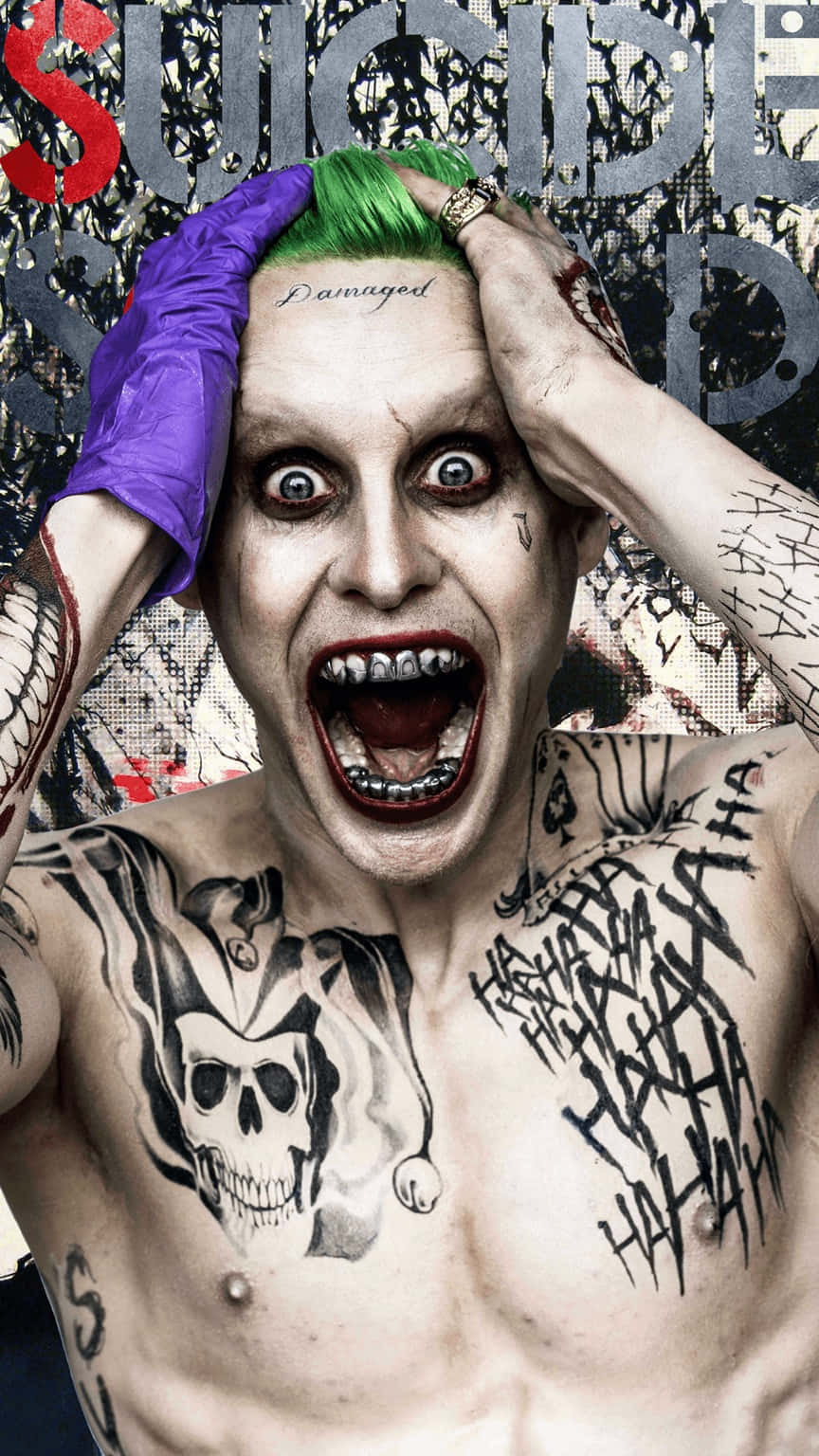 Suicide Squad 桌布 壁紙 — 一個怪誕的小丑，綠色頭髮，紫色手套，抓著頭靠著塗鴉牆尖叫。