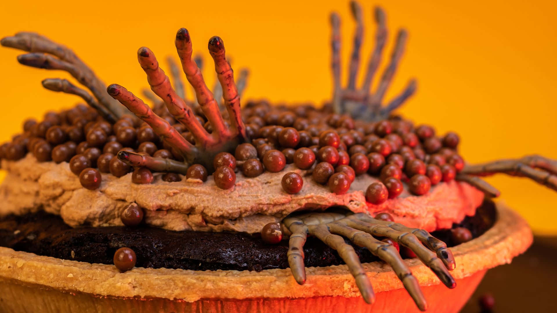 Halloween Cake 桌布 壁紙 — 一個怪誕的蛋糕，上面有殭屍手和紅色漿果，背景是鮮豔的橙色。