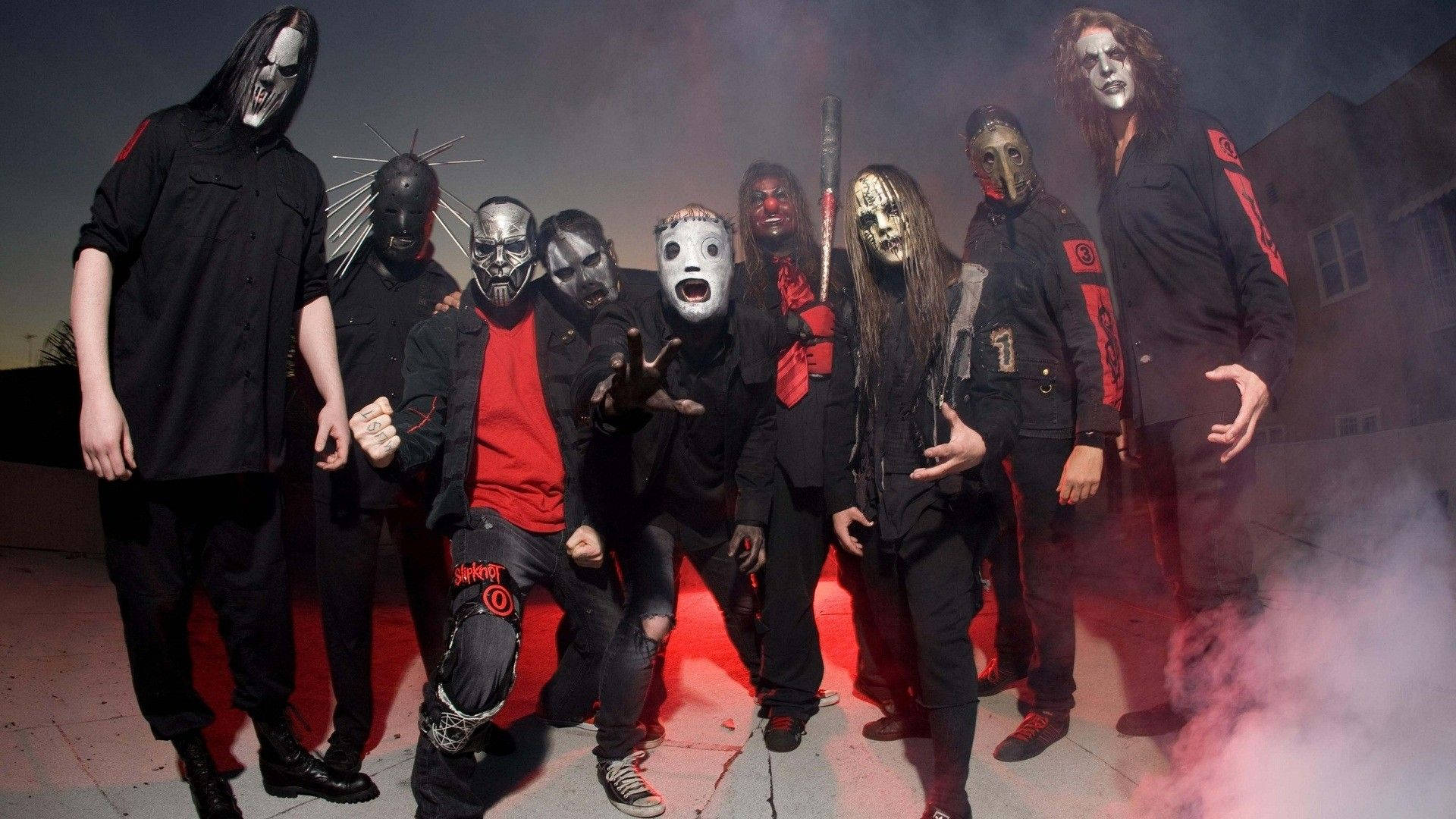 Joey Jordison 桌布 壁紙 — 一個恐怖樂團戴著怪誕面具和黑色服裝，在佈滿紅煙和燈光的屋頂上威脅性地擺姿勢。