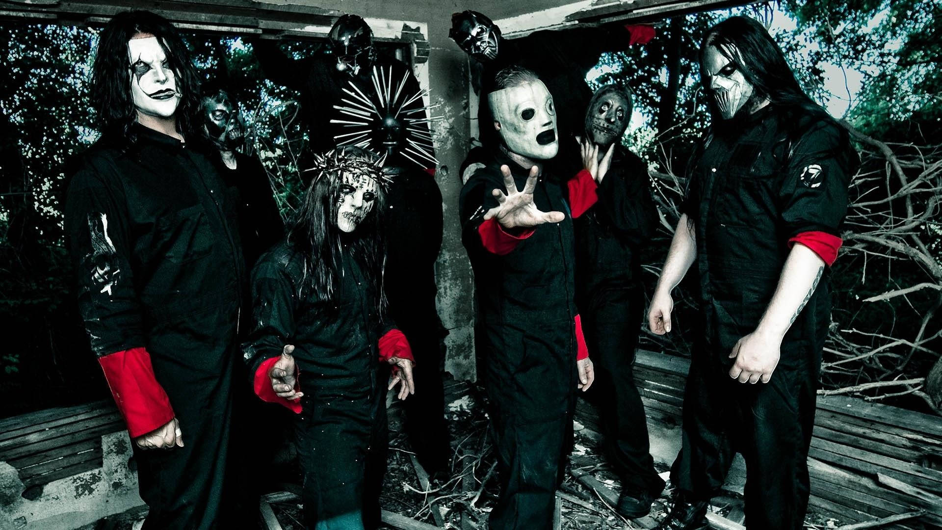 Joey Jordison 桌布 壁紙 — 一個恐怖樂團穿著黑色服裝搭配紅色點綴和怪誕面具，在破敗的戶外廢墟中擺出威脅姿勢。