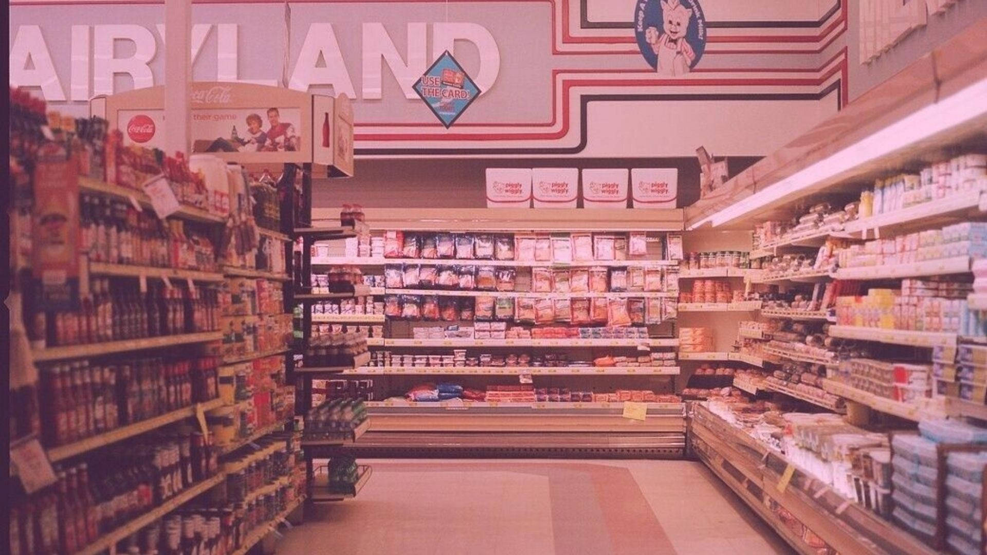 Store 桌布 壁紙 — 一個懷舊的1980年代超市通道，在溫暖的螢光燈下，有明亮的標誌和貨架。