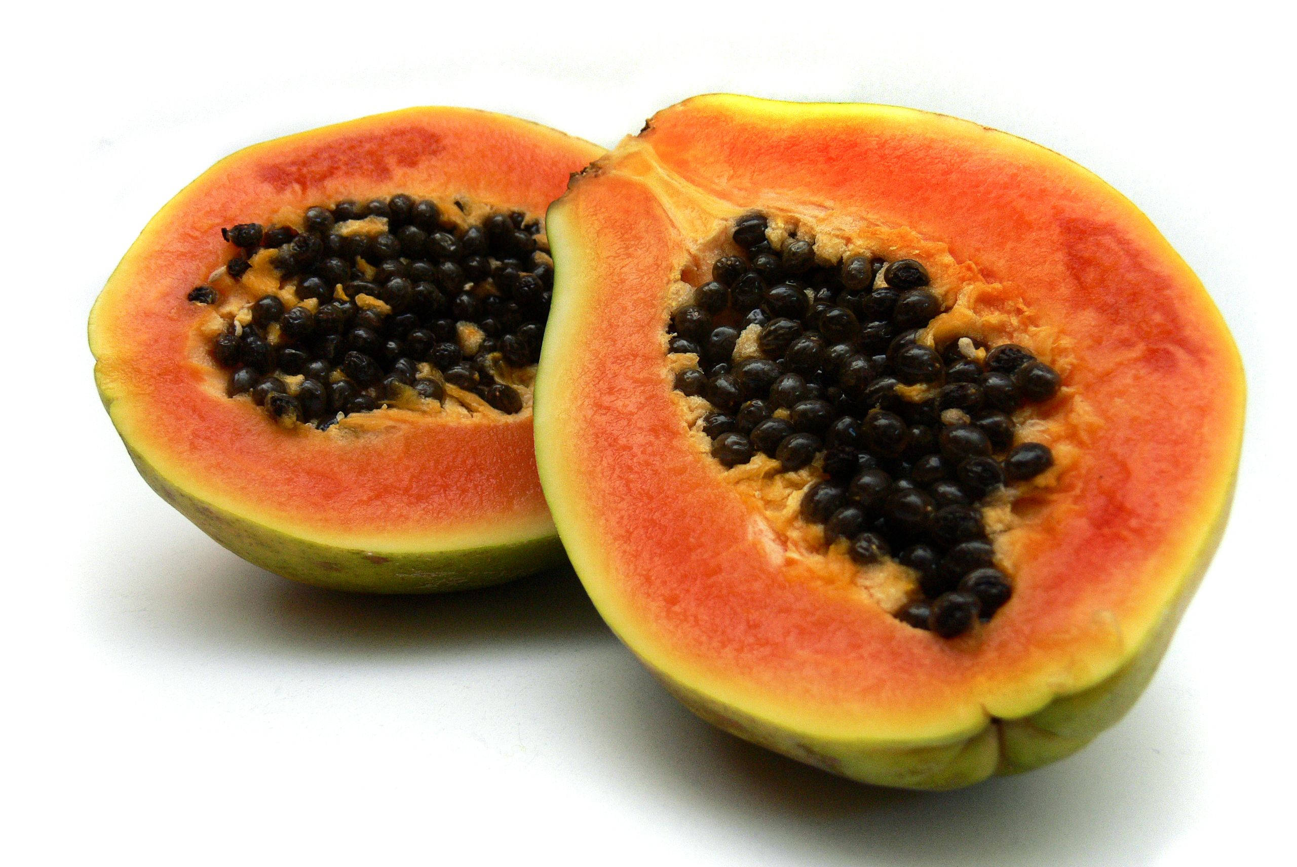 Fruits 桌布 壁紙 — 一個成熟的木瓜切開兩半，露出多汁的橙色果肉和黑色種子，背景為純白色。