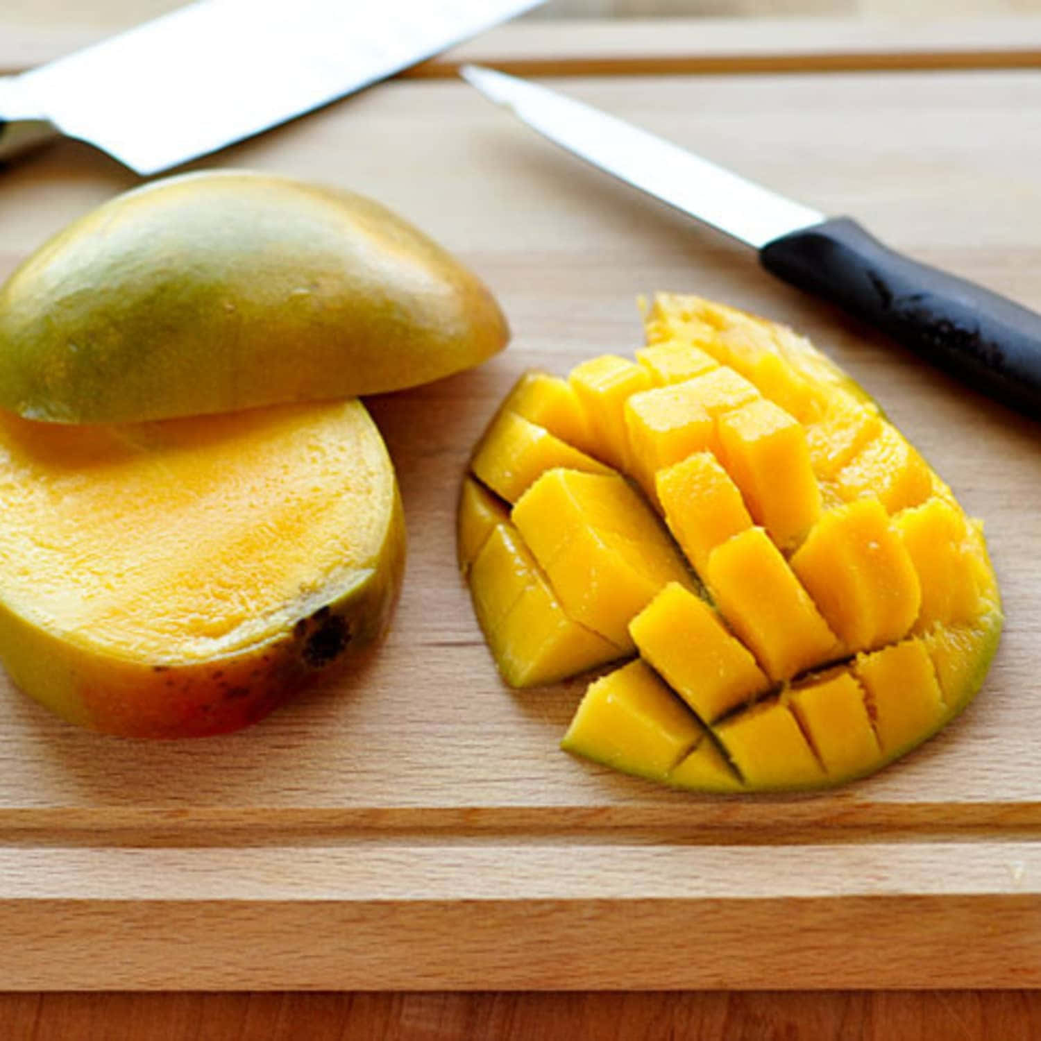 Mango 桌布 壁紙 — 一個成熟的芒果切成整齊的方塊，放在木砧板上，旁邊有半個芒果和兩把刀。