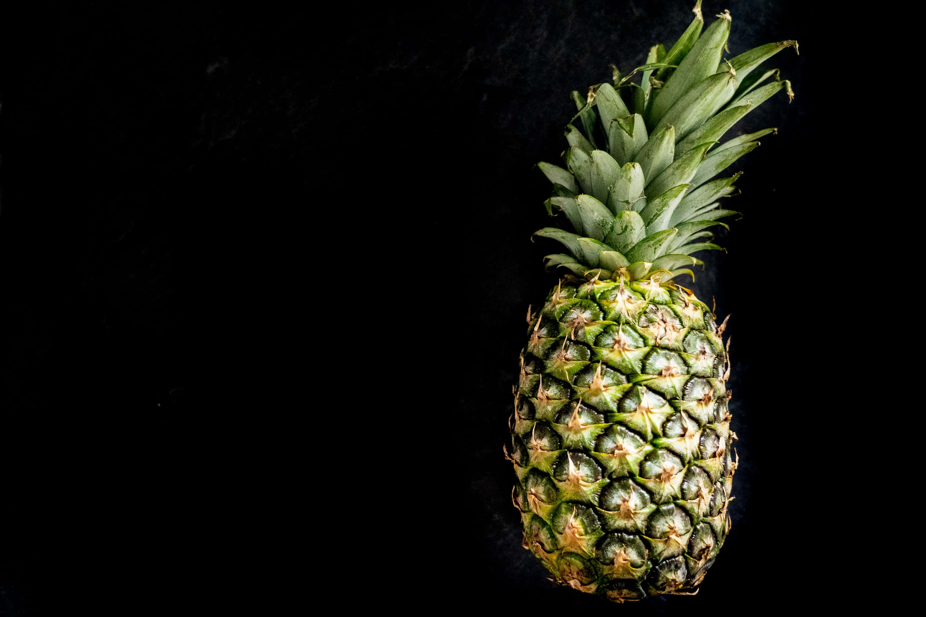 Pineapple 桌布 壁紙 — 一個成熟的鳳梨，帶有綠色冠部，孤立地立在黑色背景前。