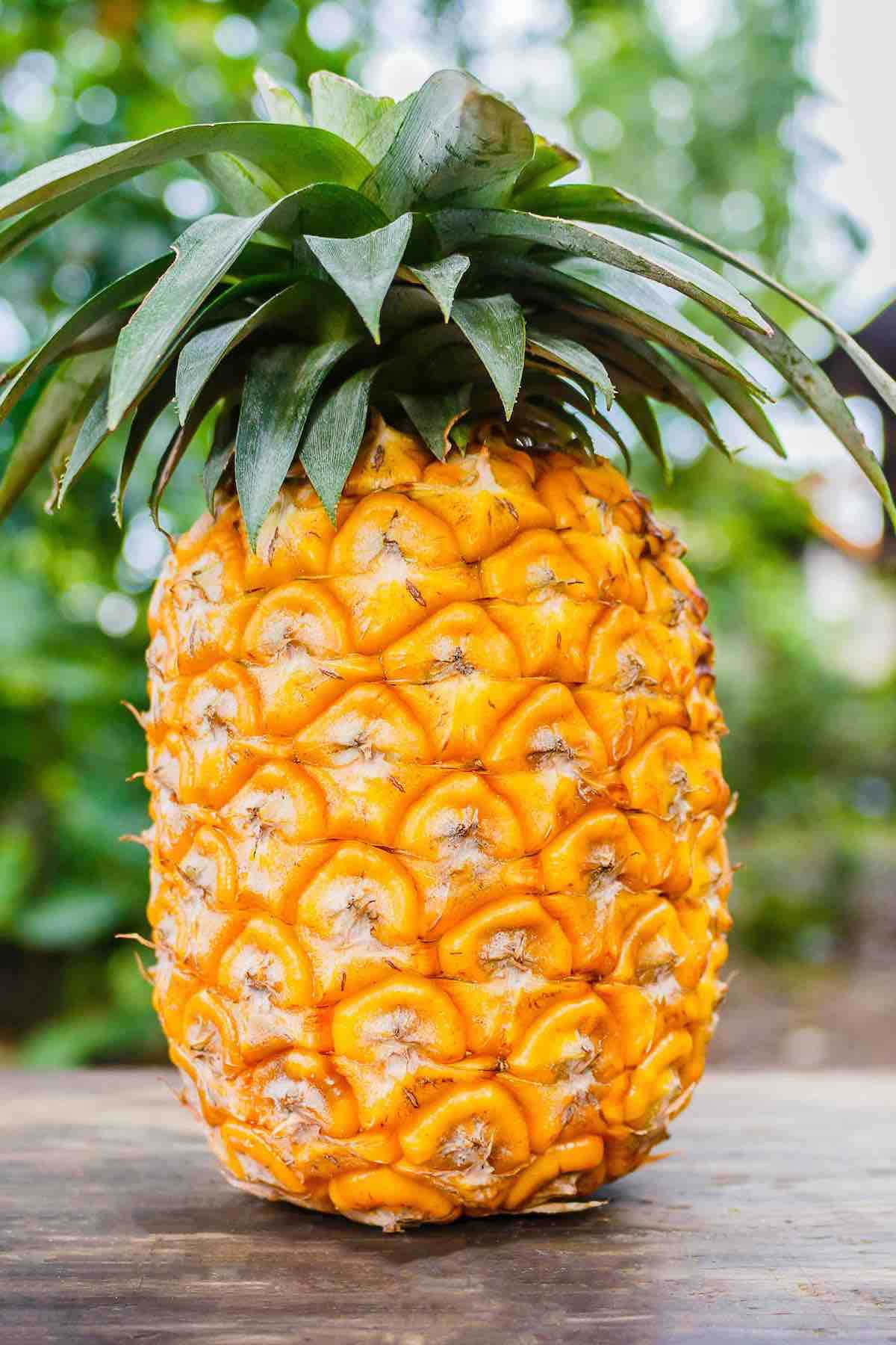 Pineapple 桌布 壁紙 — 一個成熟的鳳梨，帶有鮮黃色的果皮和綠色的冠，放在木質表面上，背景是模糊的綠色。