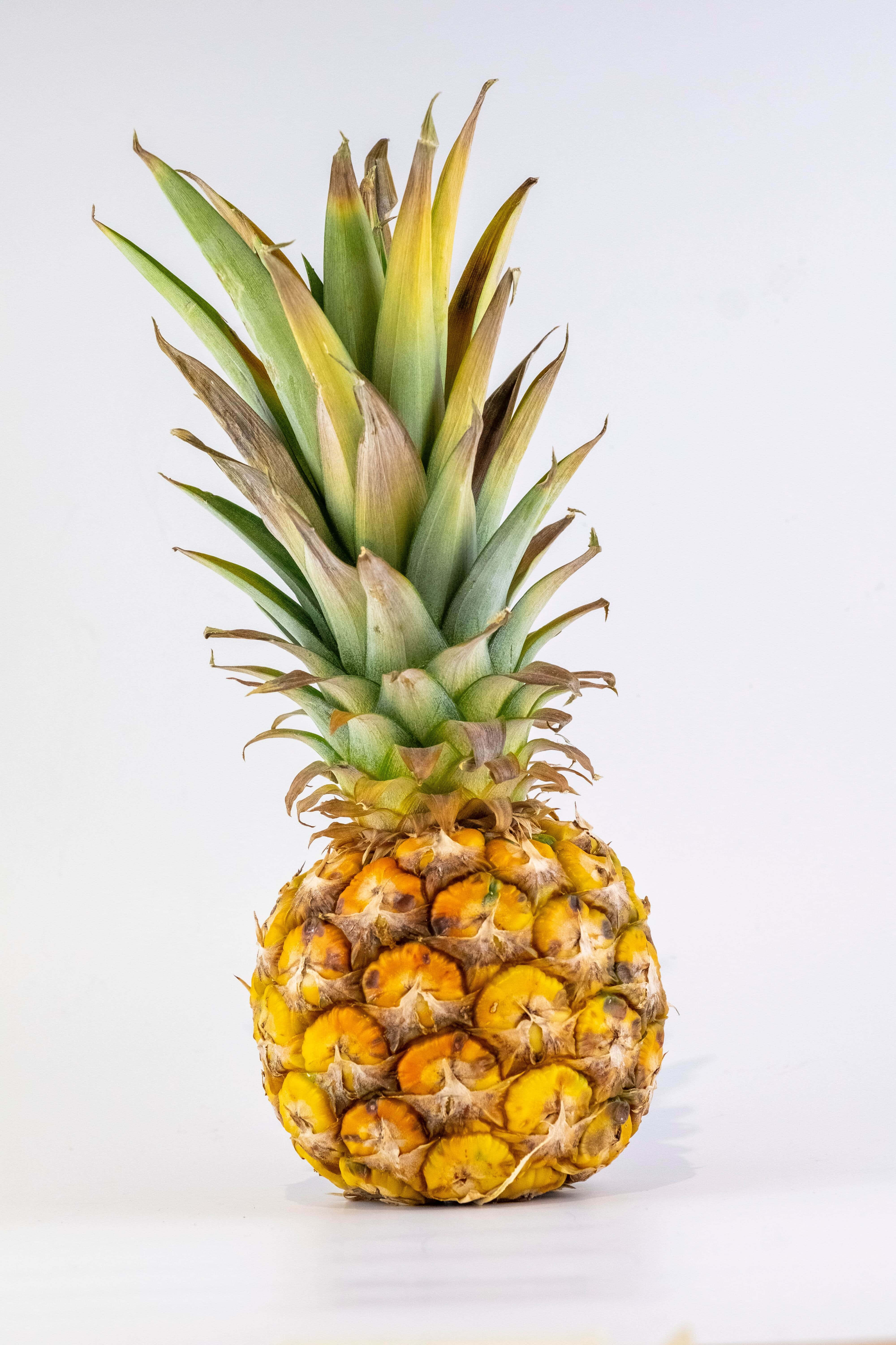 Pineapple 桌布 壁紙 — 一個成熟的鳳梨，金黃色的外皮和綠色的尖刺冠，孤立在明亮的白色表面上。