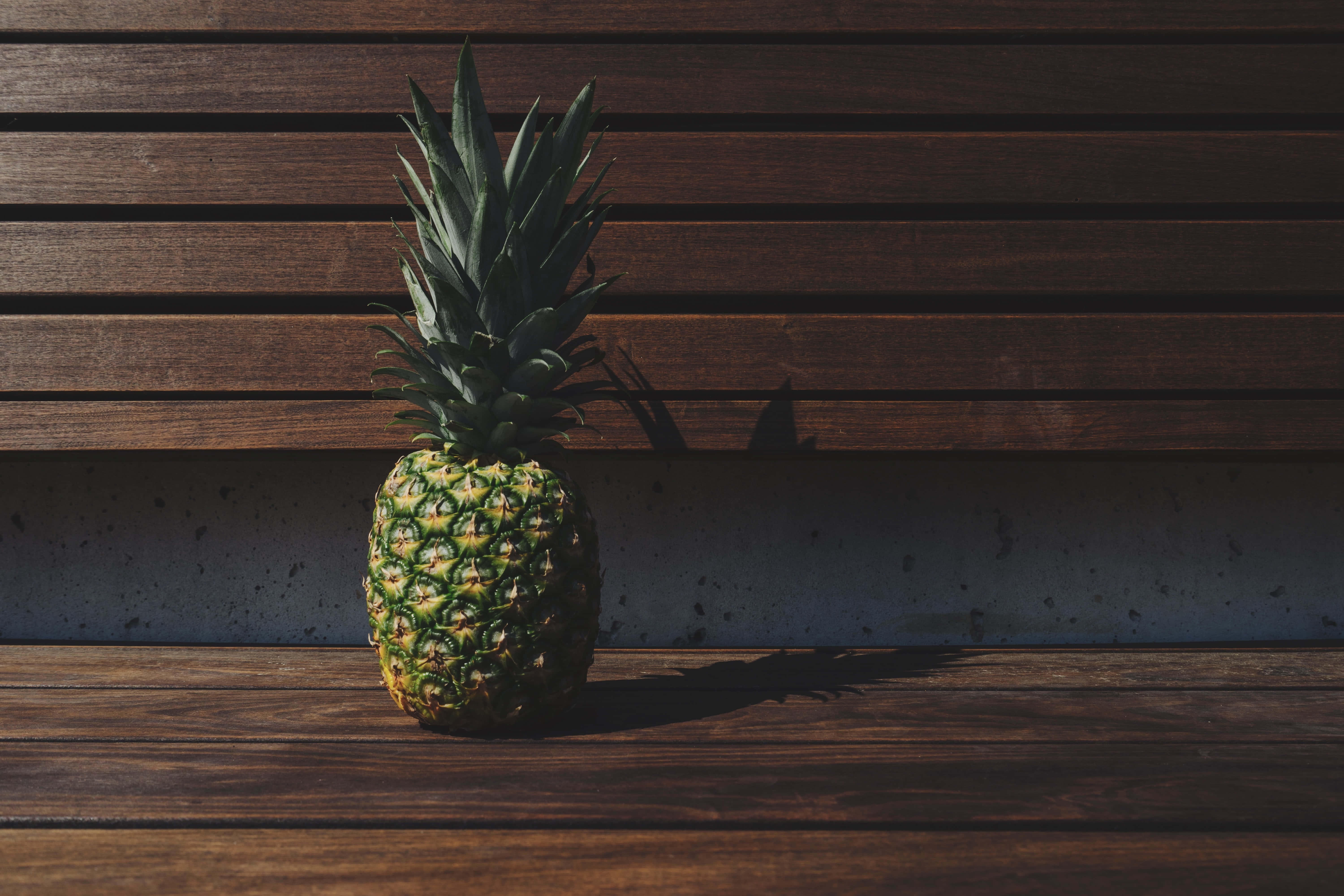 Pineapple 桌布 壁紙 — 一個成熟的鳳梨在溫暖的陽光下，靠著混凝土牆，放在木長椅上。